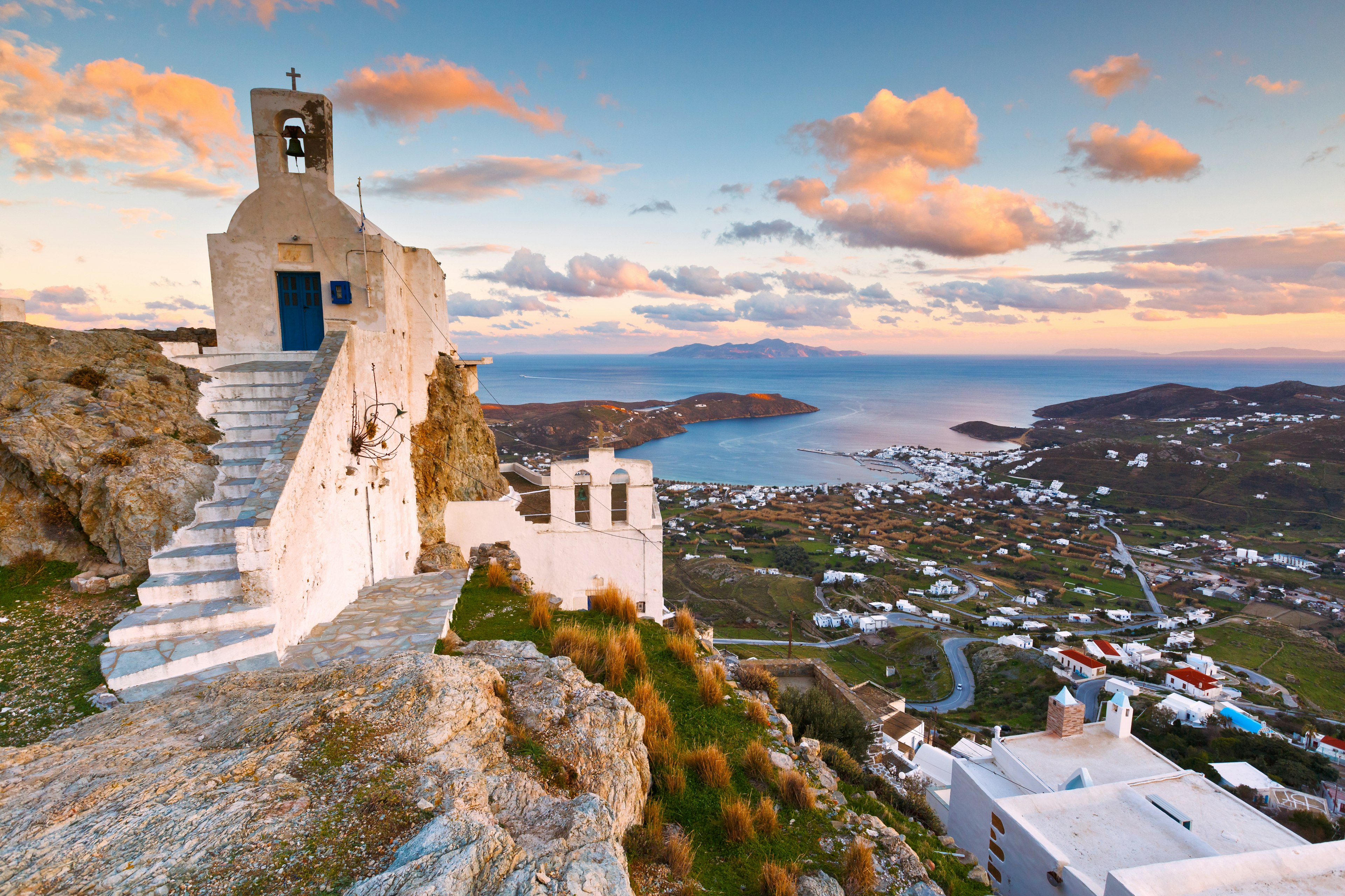 A viewpoint with a small chapel in the foreground and a vast view down to the small harbor, sea and distant islands