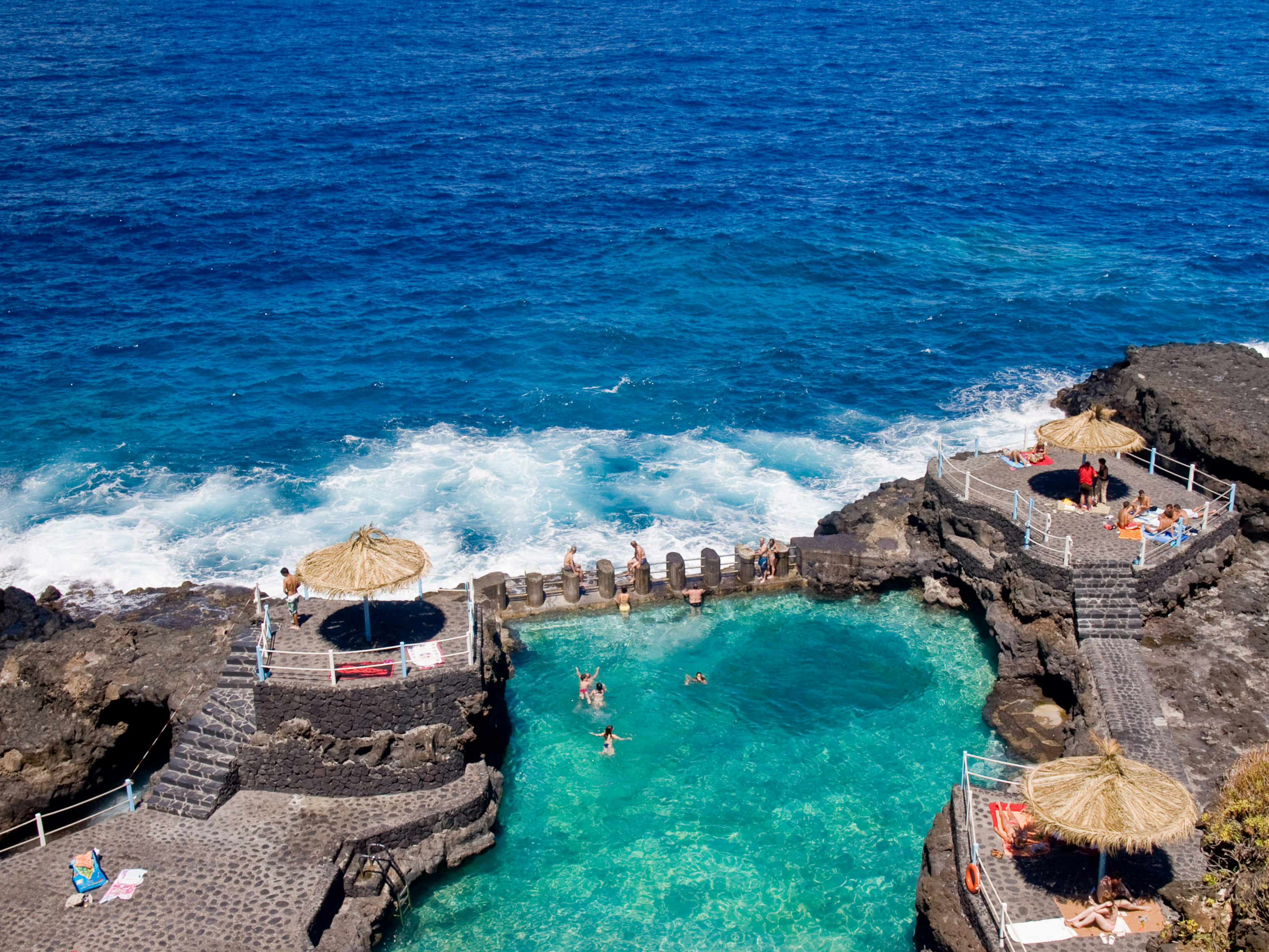 People swim in a sea pool on a black volanic beach in La Palma.