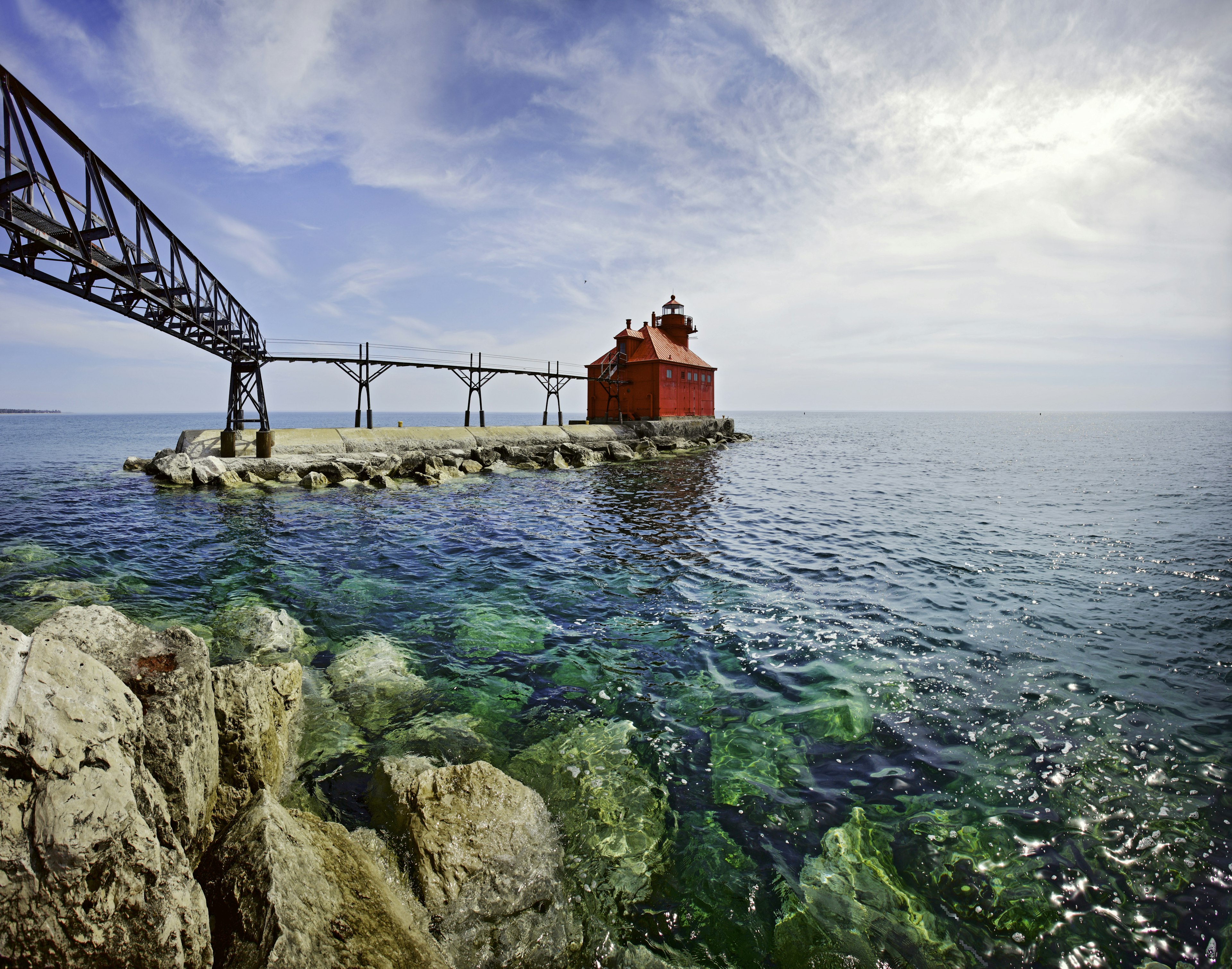 A red squat lighthouse building at the edge of pier leading out into a lake