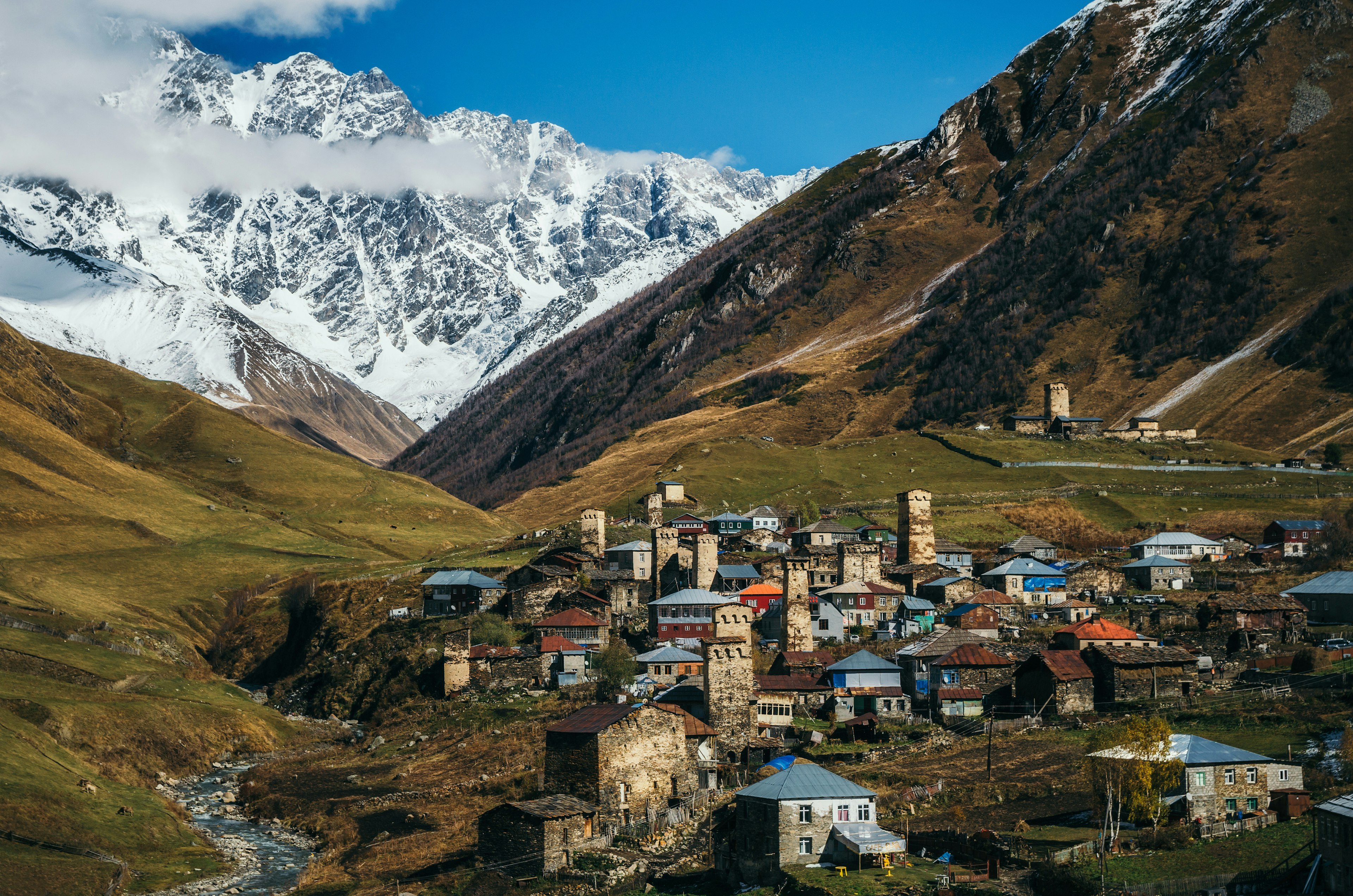 A remote mountain village is surrounded by steep hills and mountains, and there's a variety of different buildings including unique stone towers.