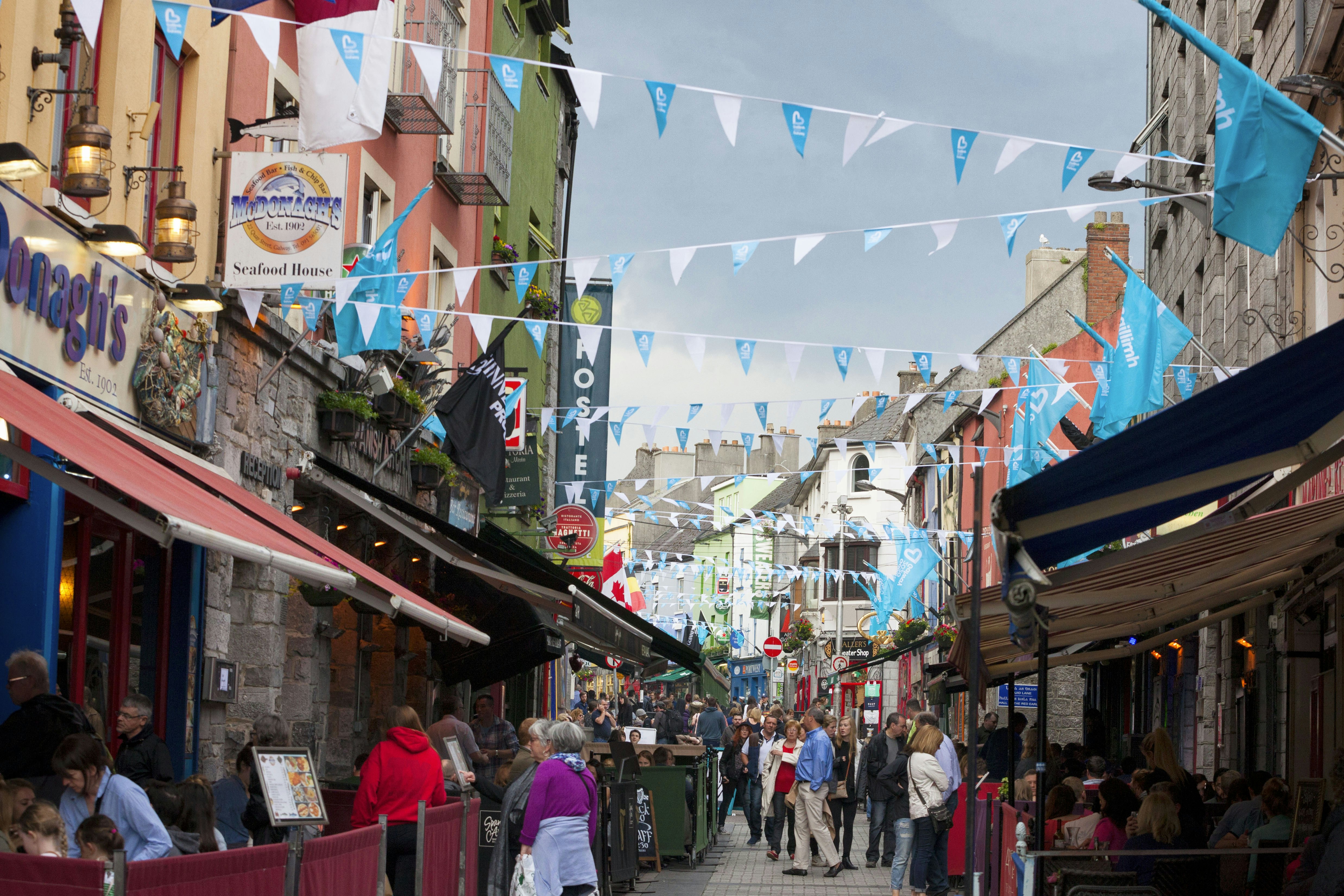 People walking along Shop Street, with colorful shops and bunting, in Galway during the day