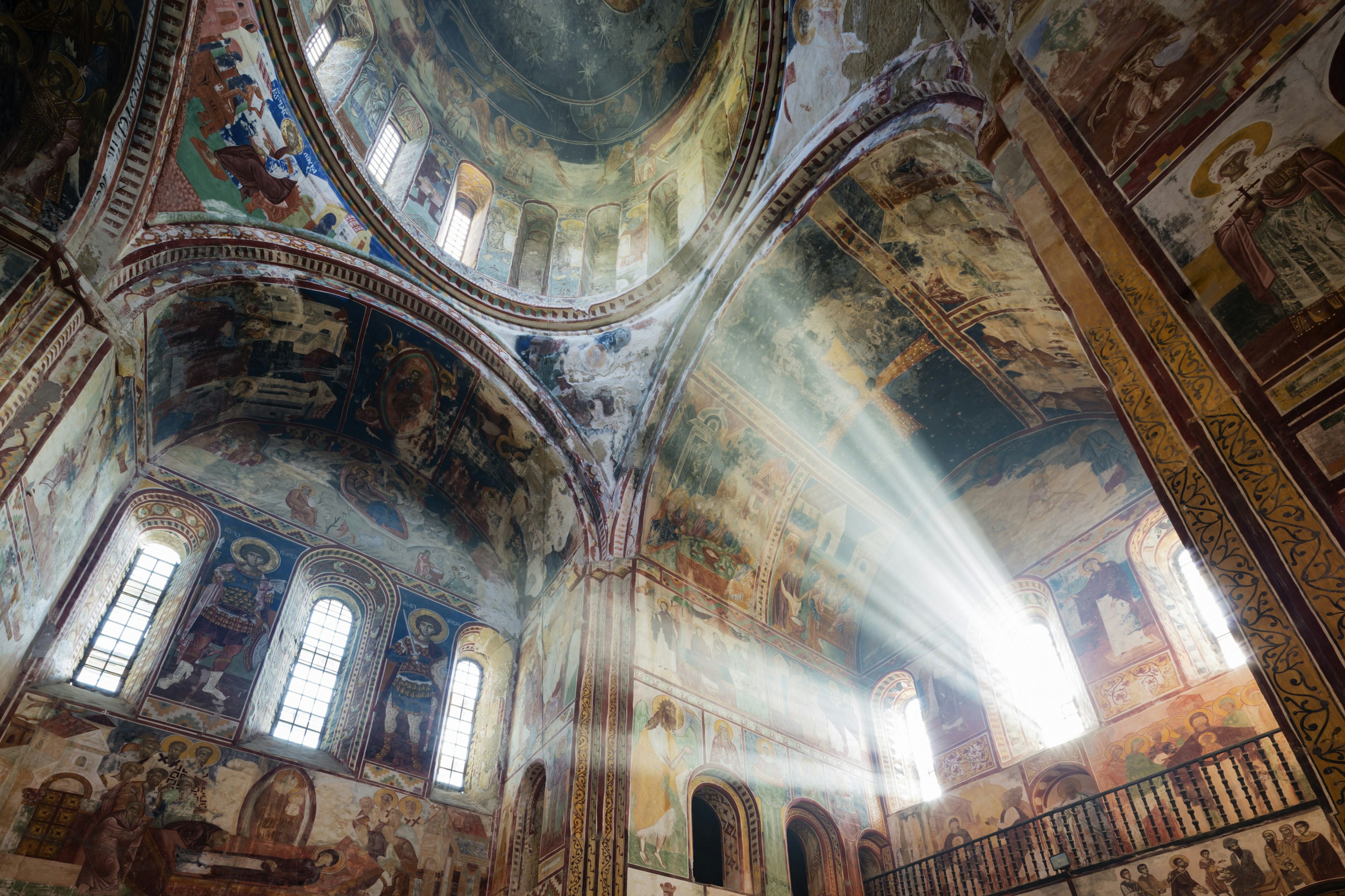 Upwards angle towards the dome inside Unesco-listed Gelati Monastery, showing colourful religious frescoes preserved on the walls and ceilings inside