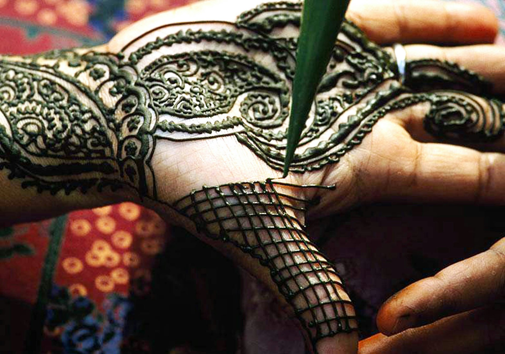 An artist designing a henna tattoo on a woman's hand in Dubai.