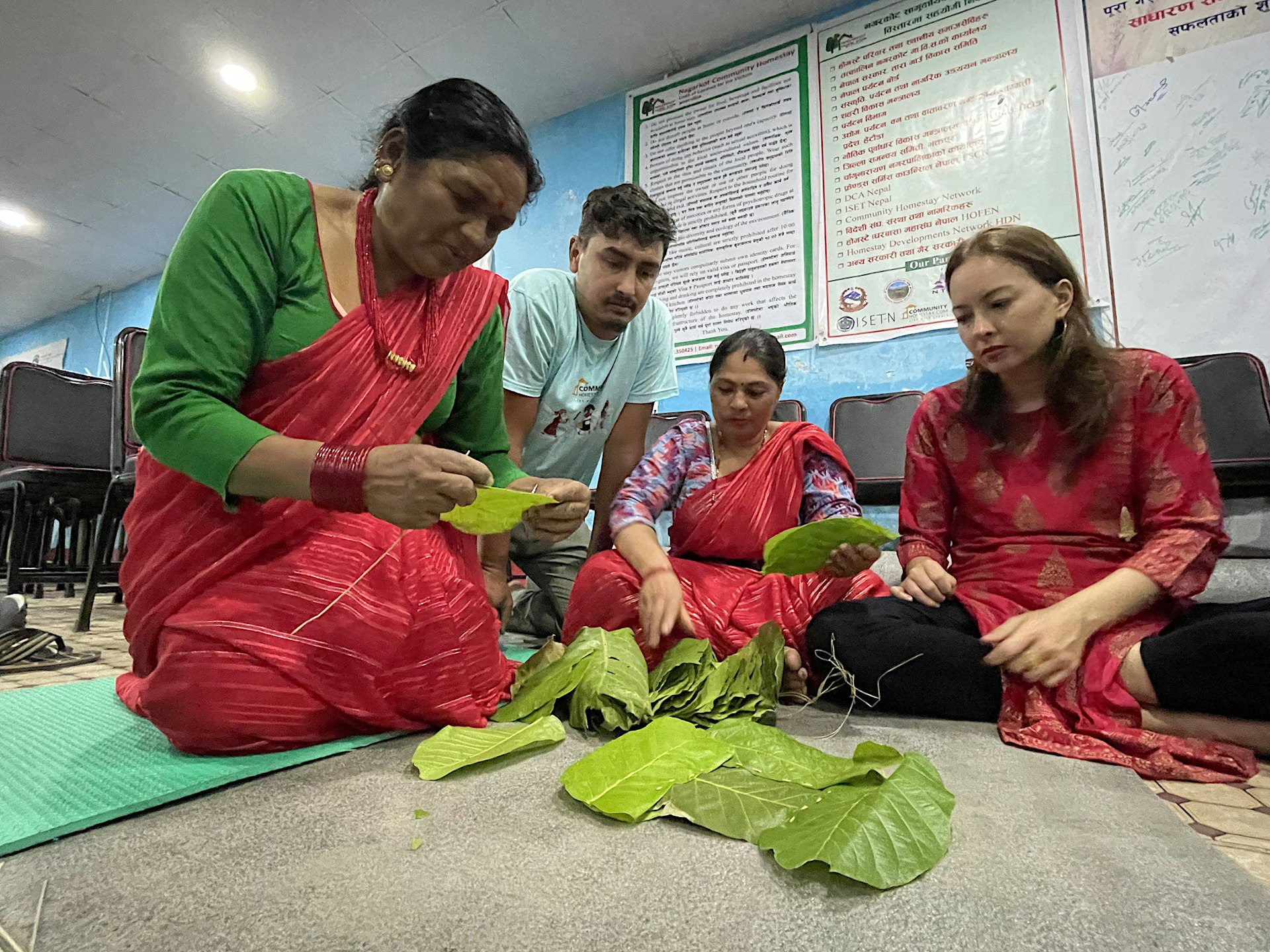 Two people demonstrate how to stitch together large green leaves to form a plate