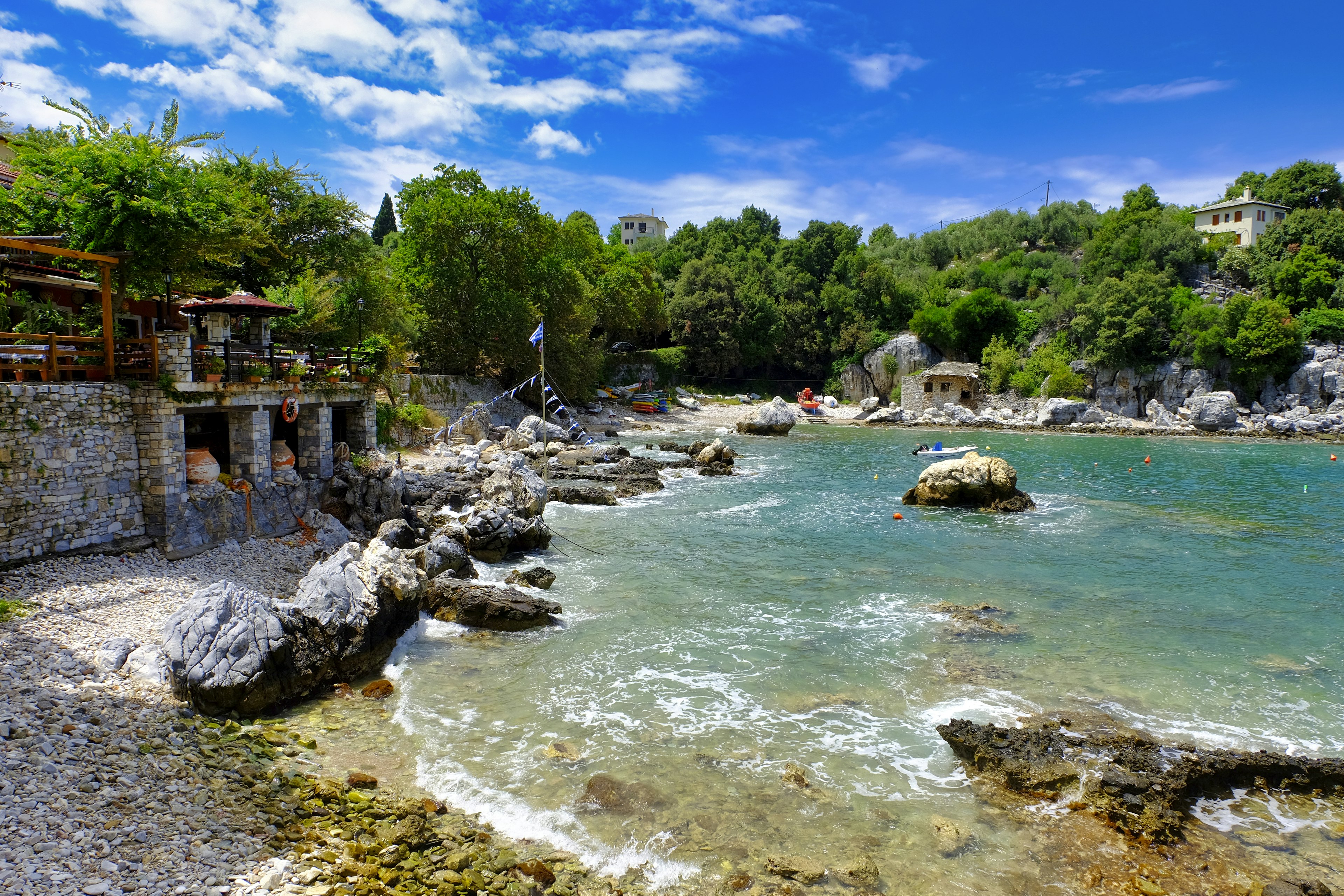 Stone buildings sit on the edge of a light blue coast.