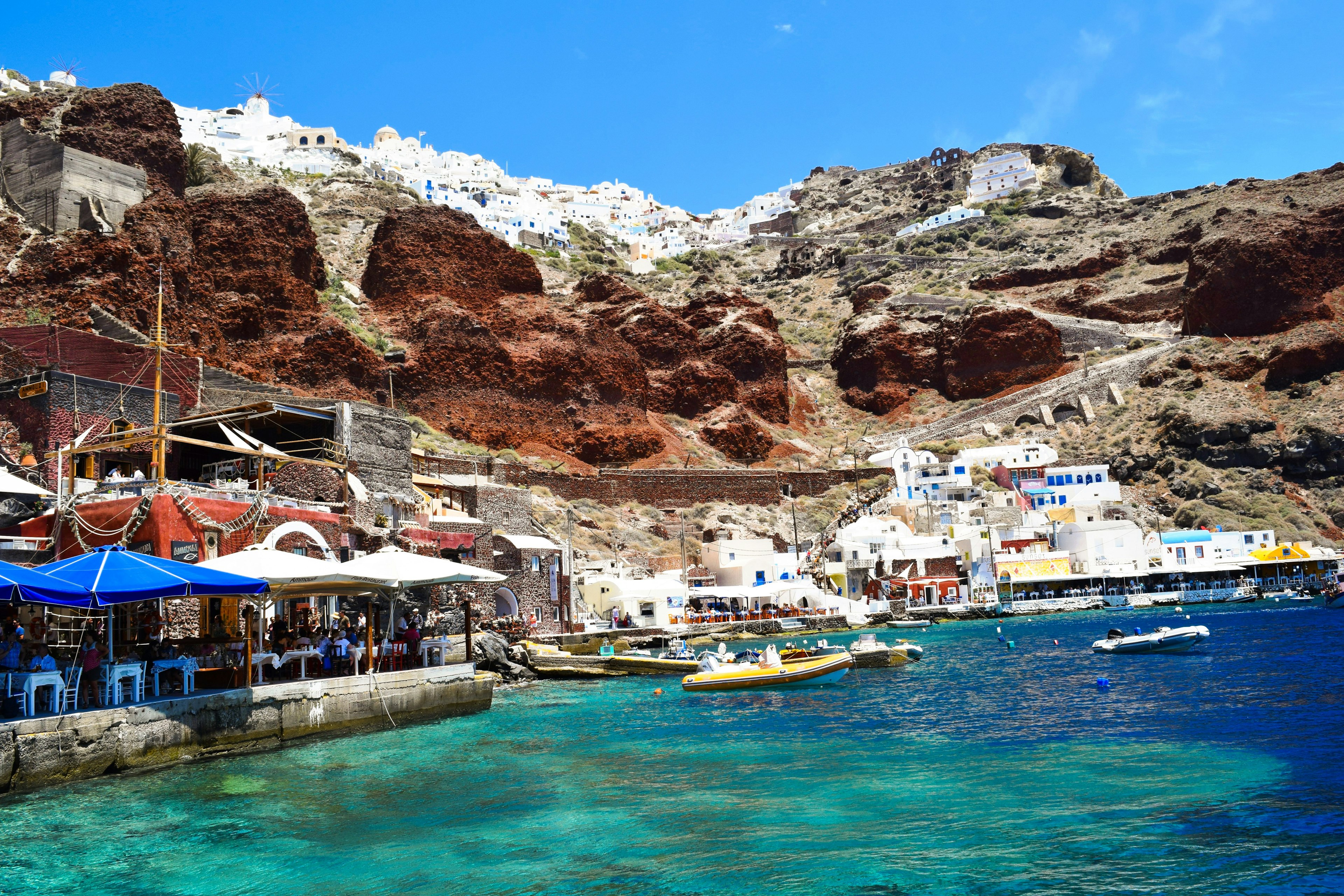 A bay with several boats. The turquoise waters contrast with the red cliffs backing the village