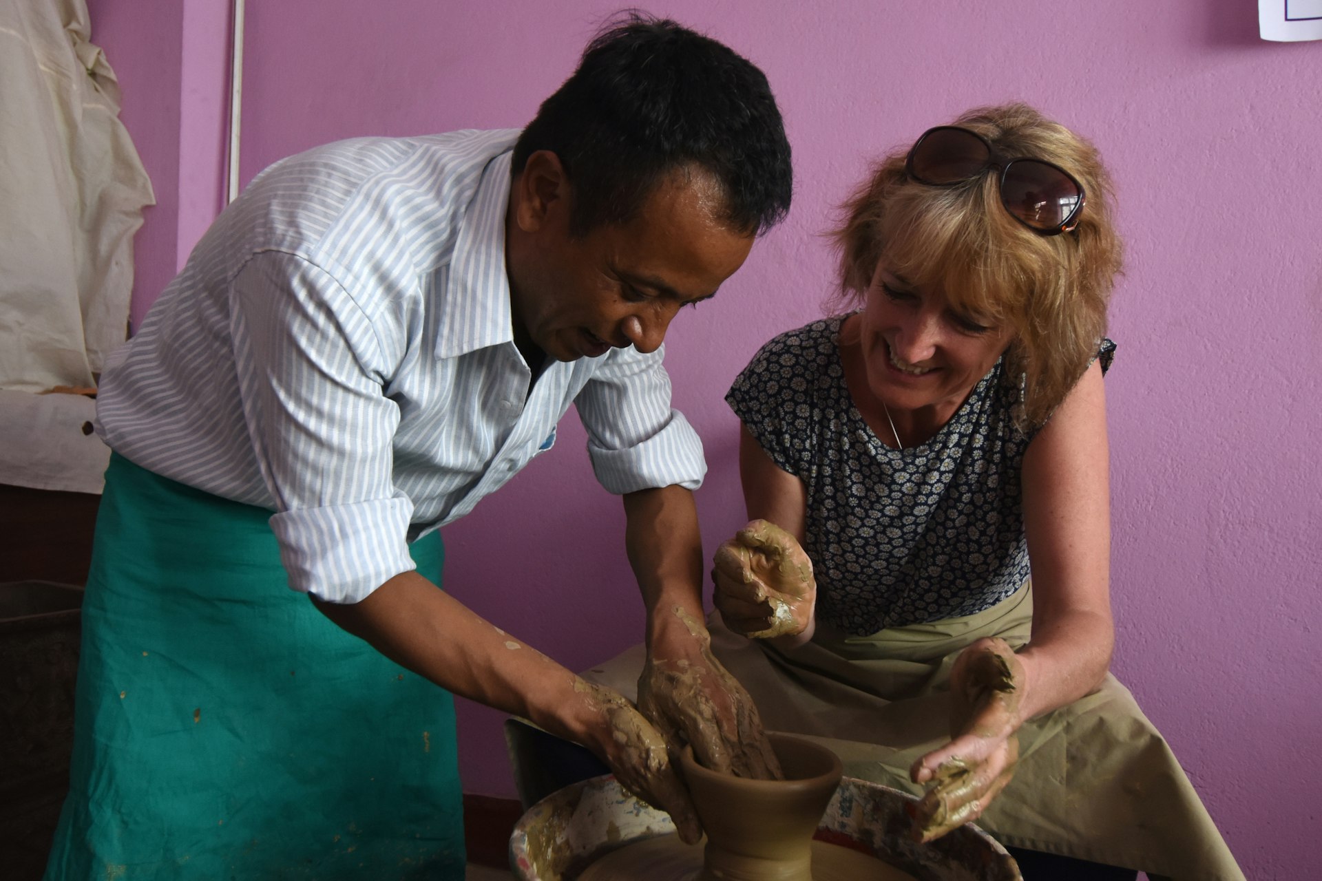 A teacher shows a student how to straighten up the edges on the pot she is making on a pottery wheel