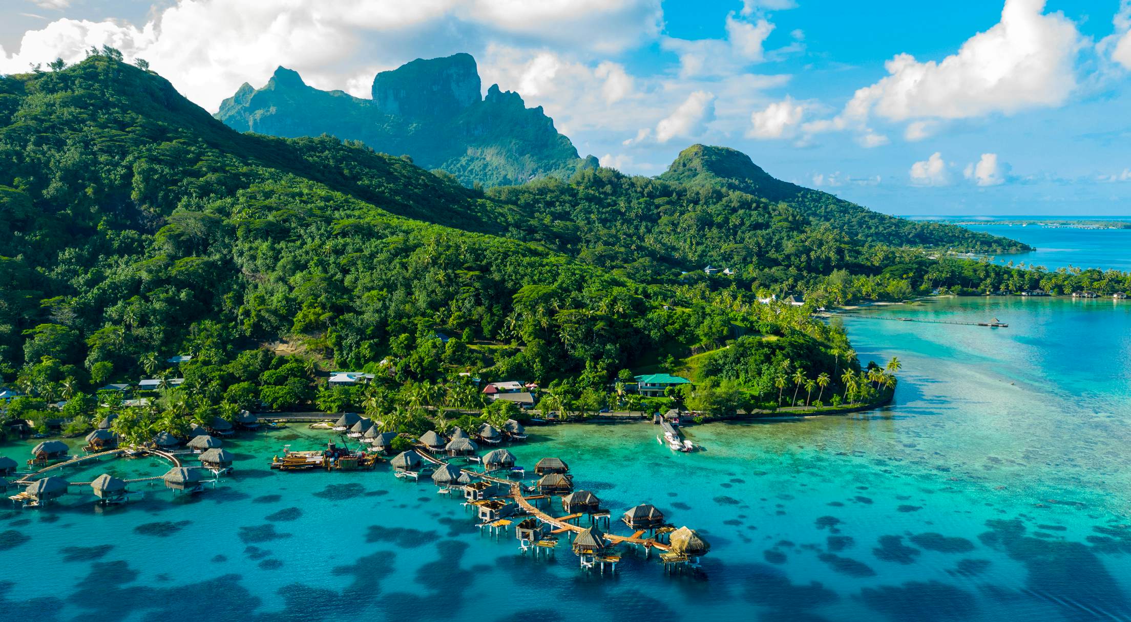 View of Bora Bora, featuring green mountains and water-front villas.