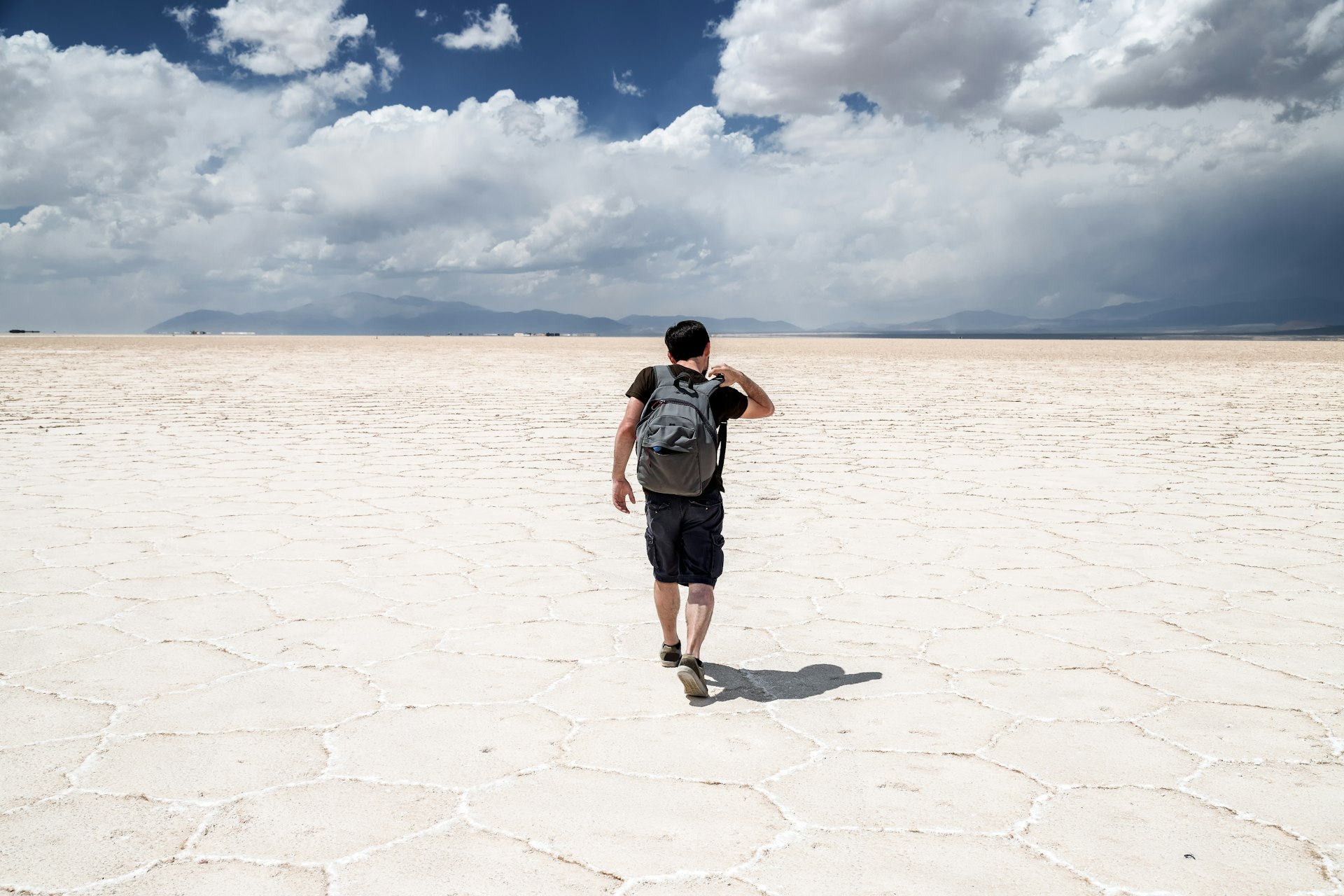 A solitary figure walks out on vast salt flats, white flat land streching featureless into the distance