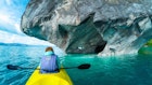 Woman sits in kayak and explores the Marble Caves and rocks on the lake of General Carrera, Chile