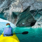 Woman sits in kayak and explores the Marble Caves and rocks on the lake of General Carrera, Chile
