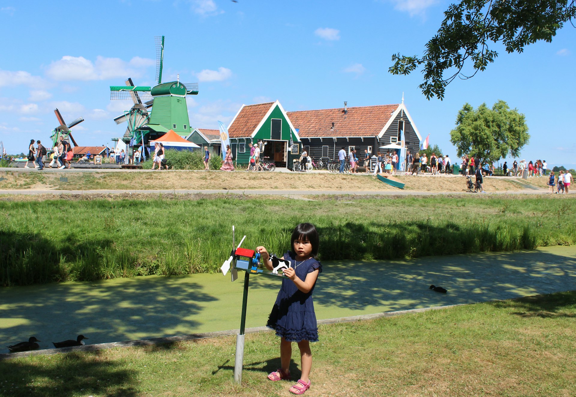 A girl plays with a toy windmill near the real windmills of Zaanse Schans, Netherlands