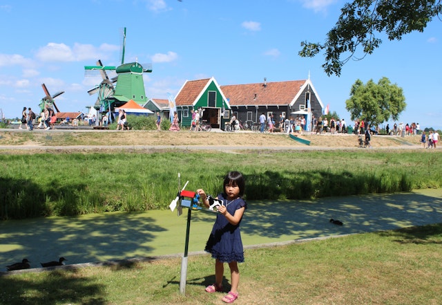 A girl plays with a toy windmill near the real windmills of Zaanse Schans, Netherlands