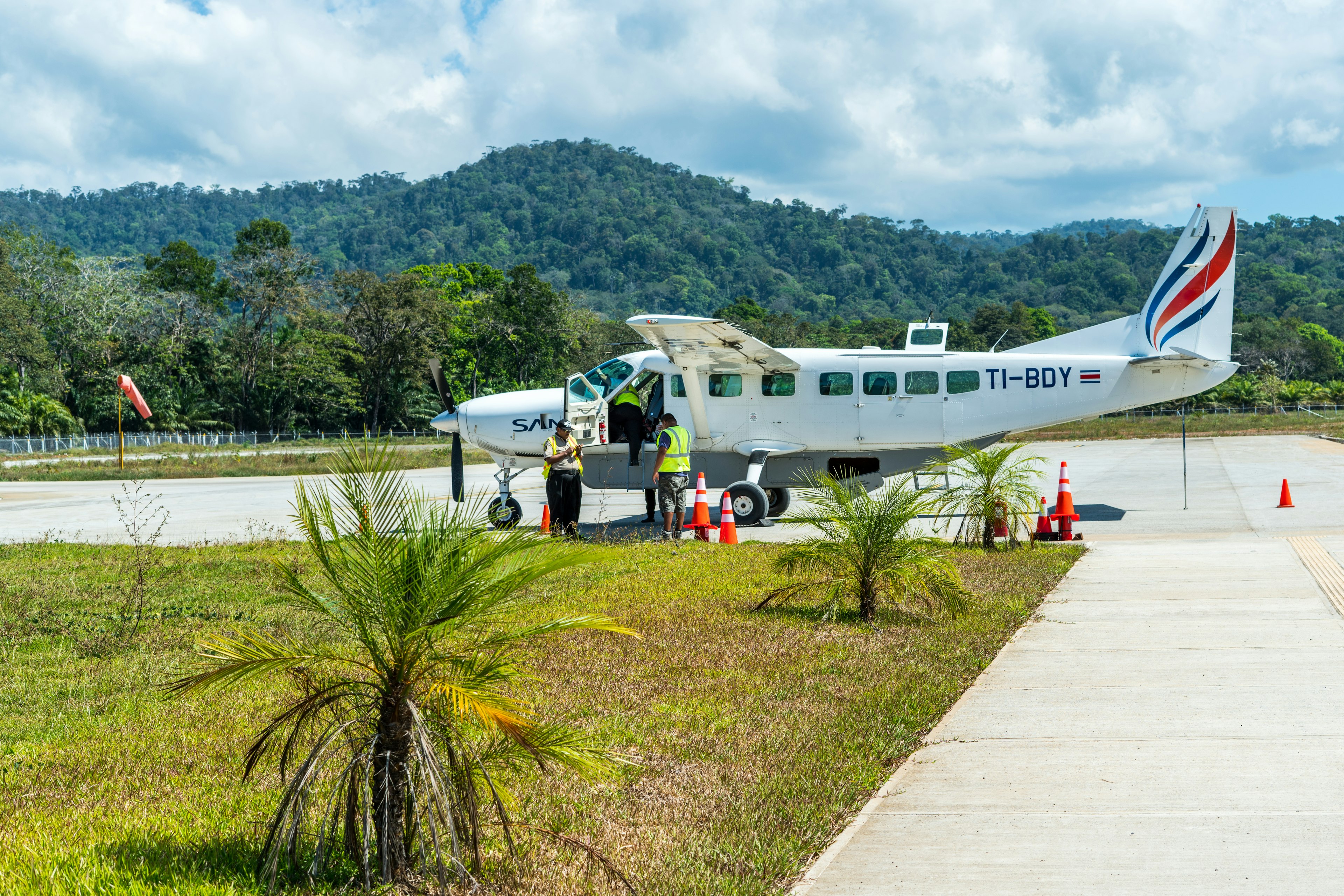 A Cessna airplane is standing on an airstrip amid a tropical landscape with rainforest in the background