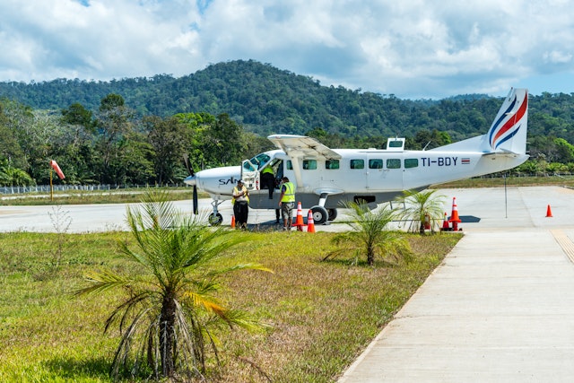 A Cessna airplane is standing on an airstrip amid a tropical landscape with rainforest in the background