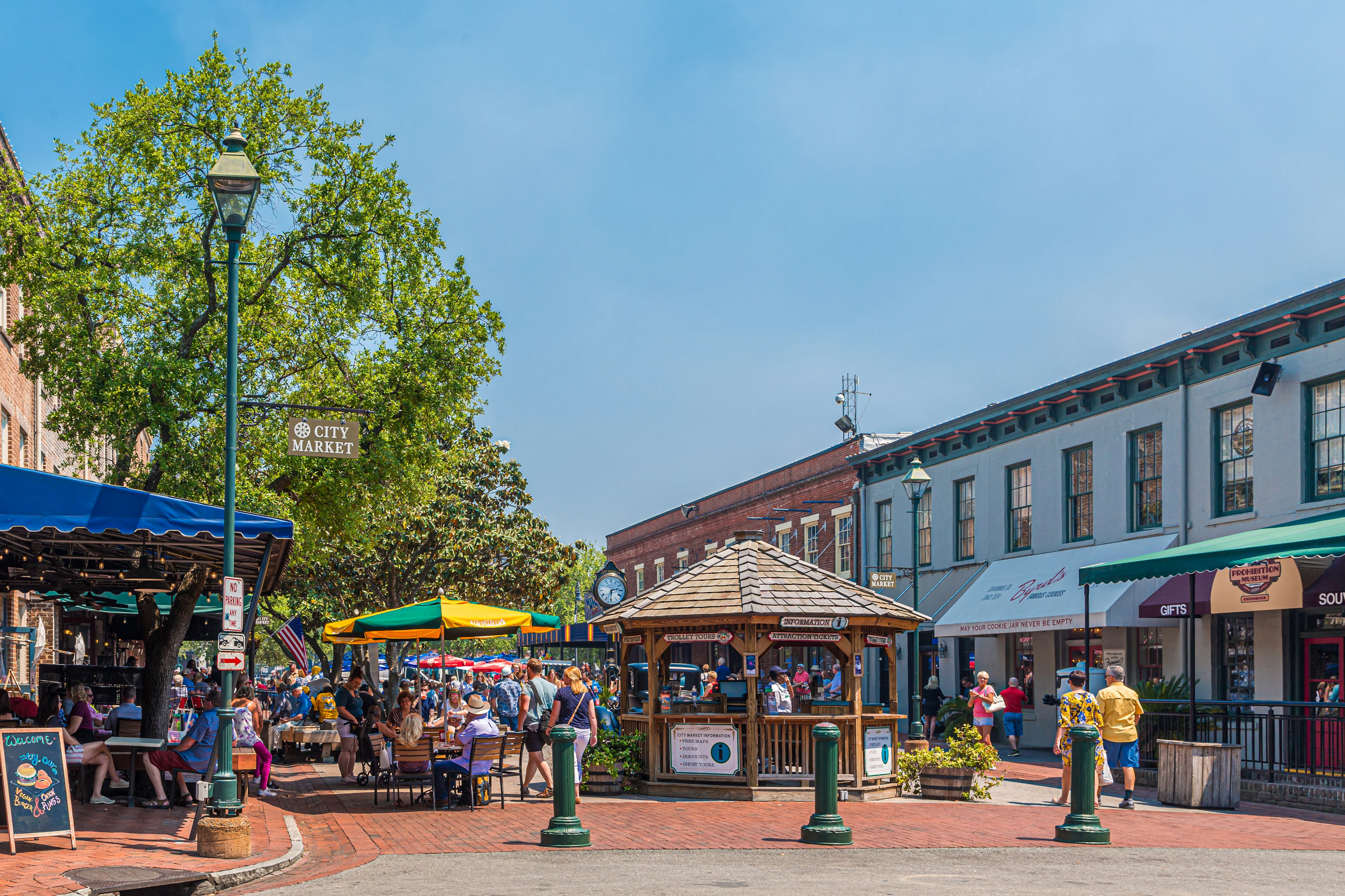 A pedestrianized street lined with shops and restaurants, with diners sat at tables outside