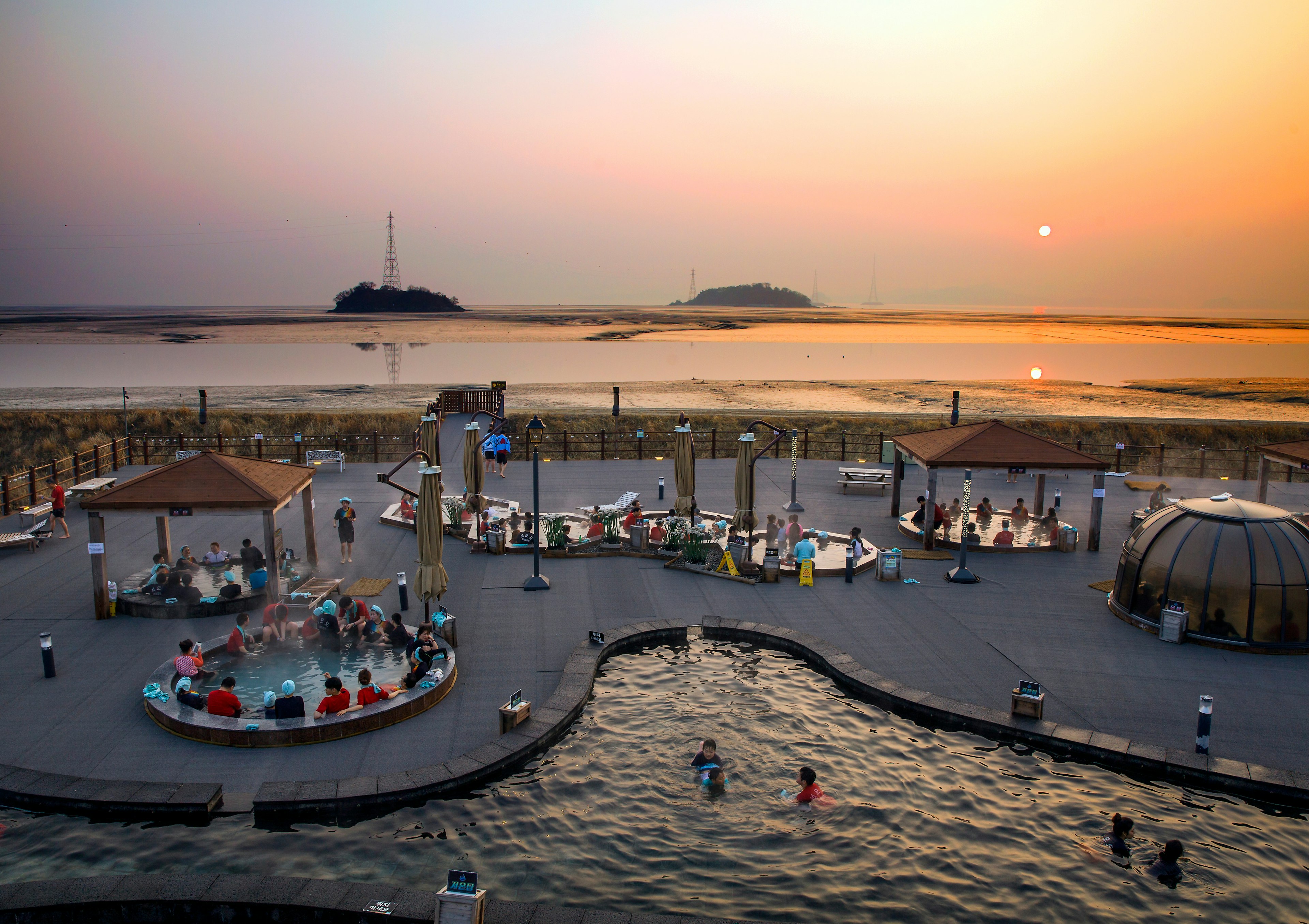 A high-angle view of a pool and several smaller hot-water pools in a coastal spa area; Sunset in the background