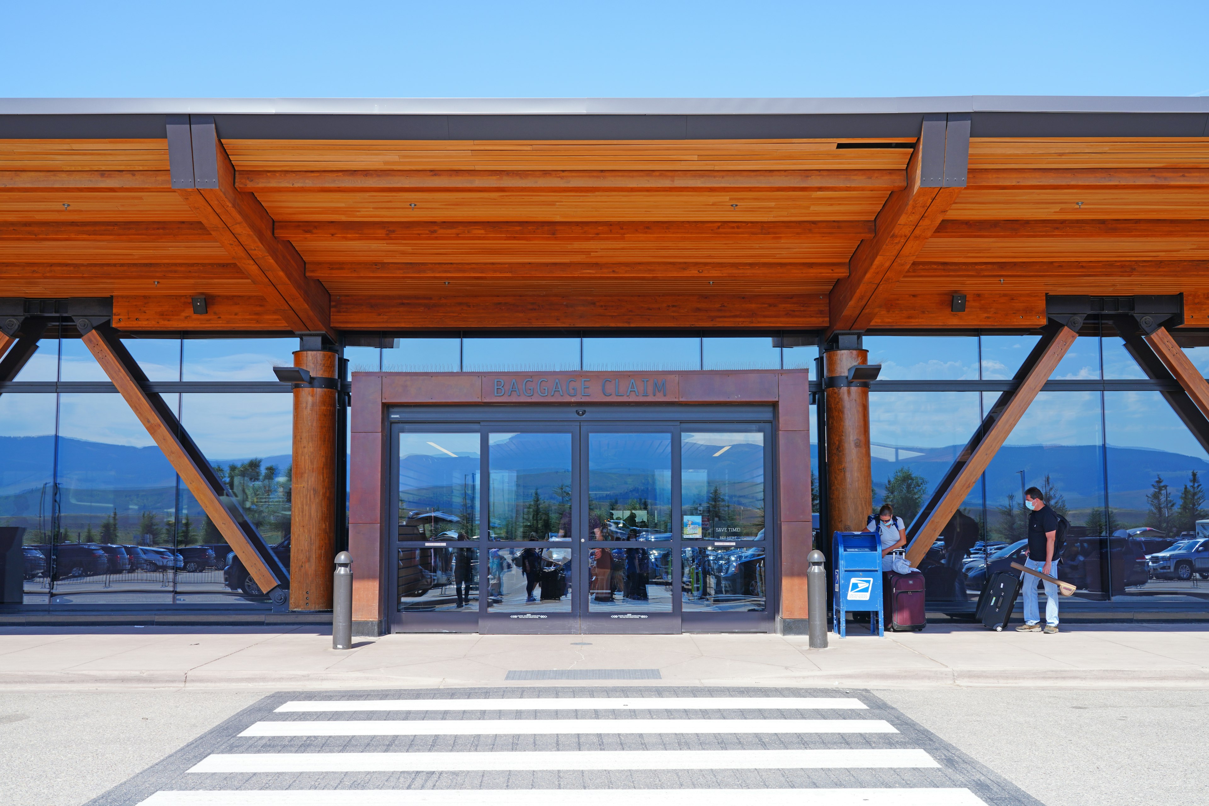 The exterior of a low-rise modernist building of glass and wood with mountains reflected in the windows