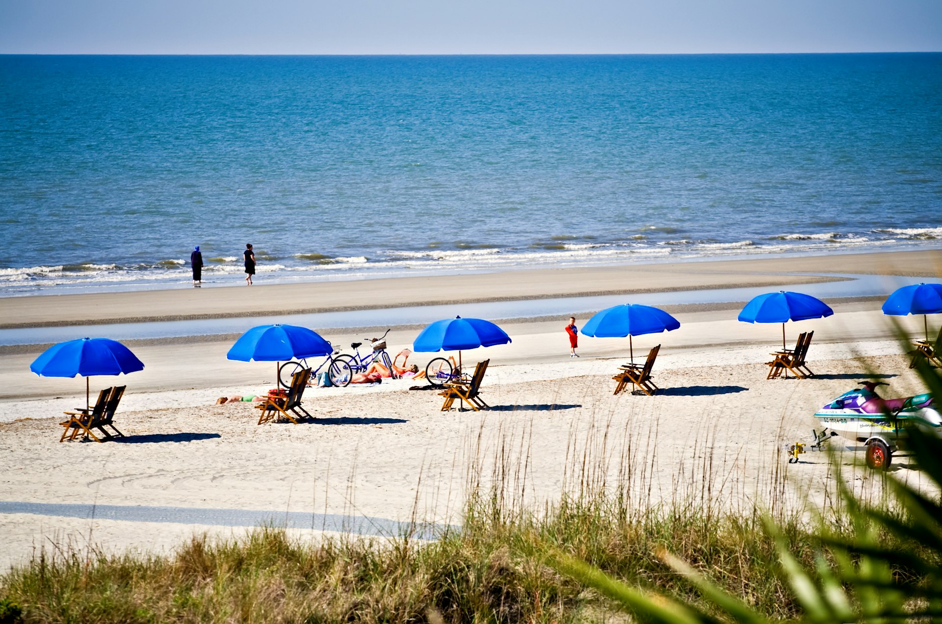 A stretch of white-sand beach with blue sun shades and people enjoying the sunshine