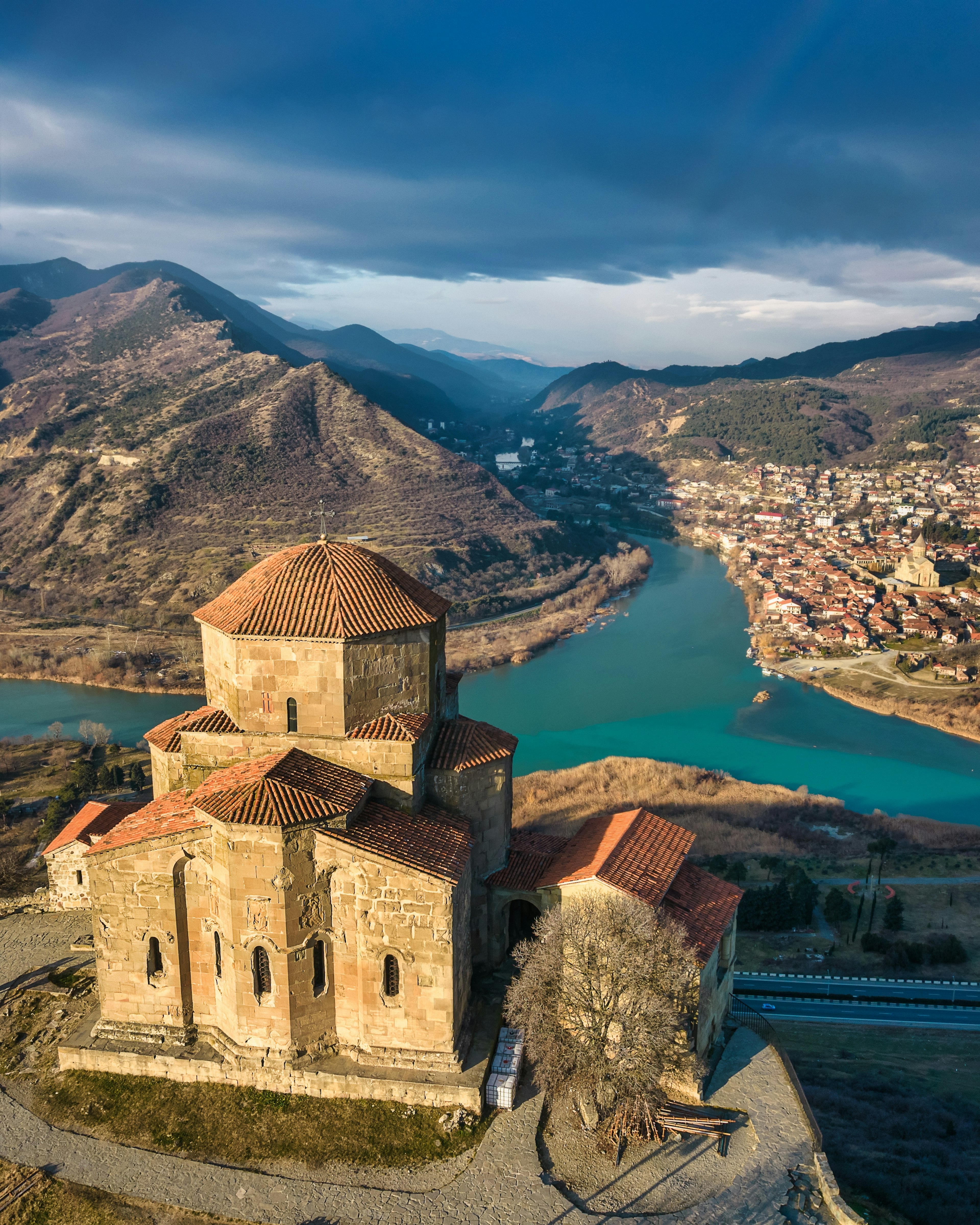 An ancient monastery stands on a hilltop; two rivers meet in the valley below, and there's a town on the opposite riverbank.