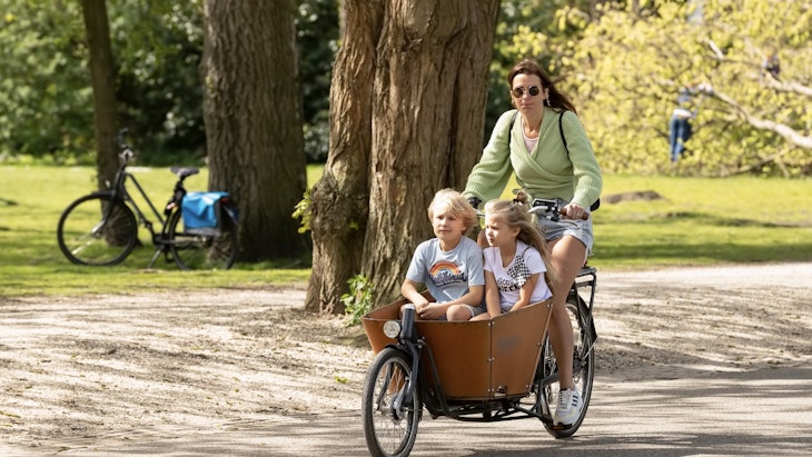 Young woman cycles with her cargo bike with children through the Vondelpark in Amsterdam