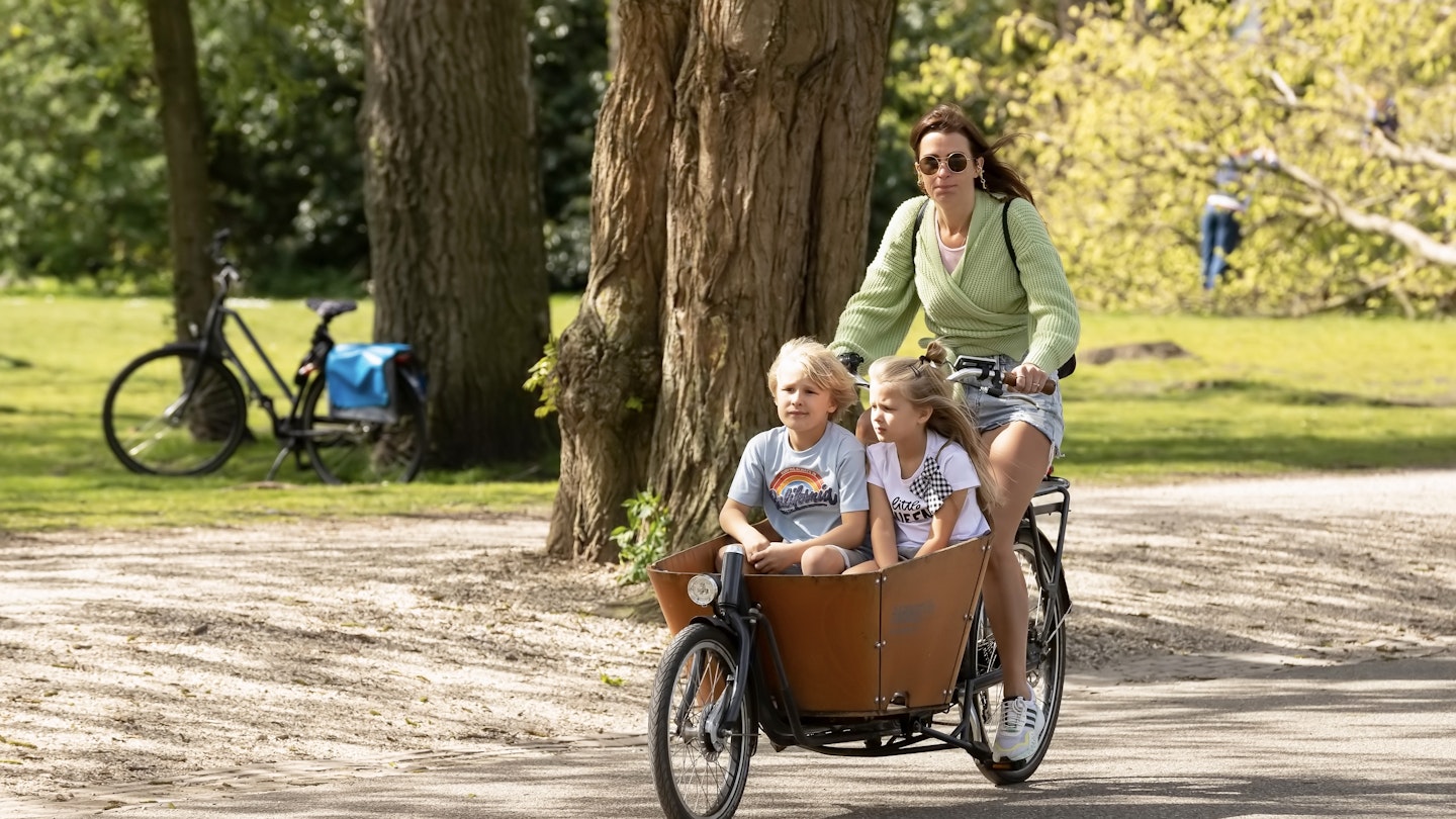 Young woman cycles with her cargo bike with children through the Vondelpark in Amsterdam