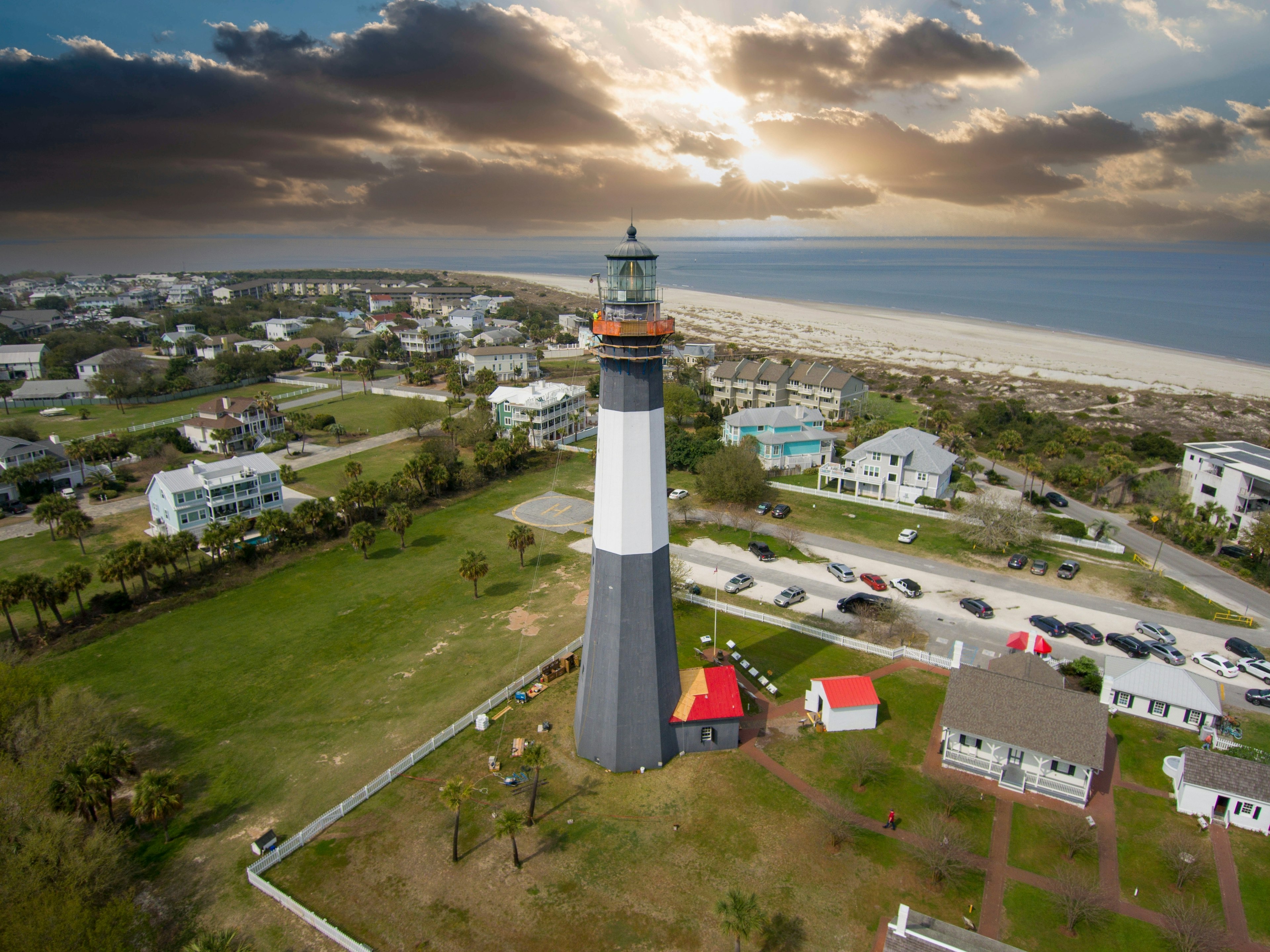 A black and white lighthouse rises above a sandy beach