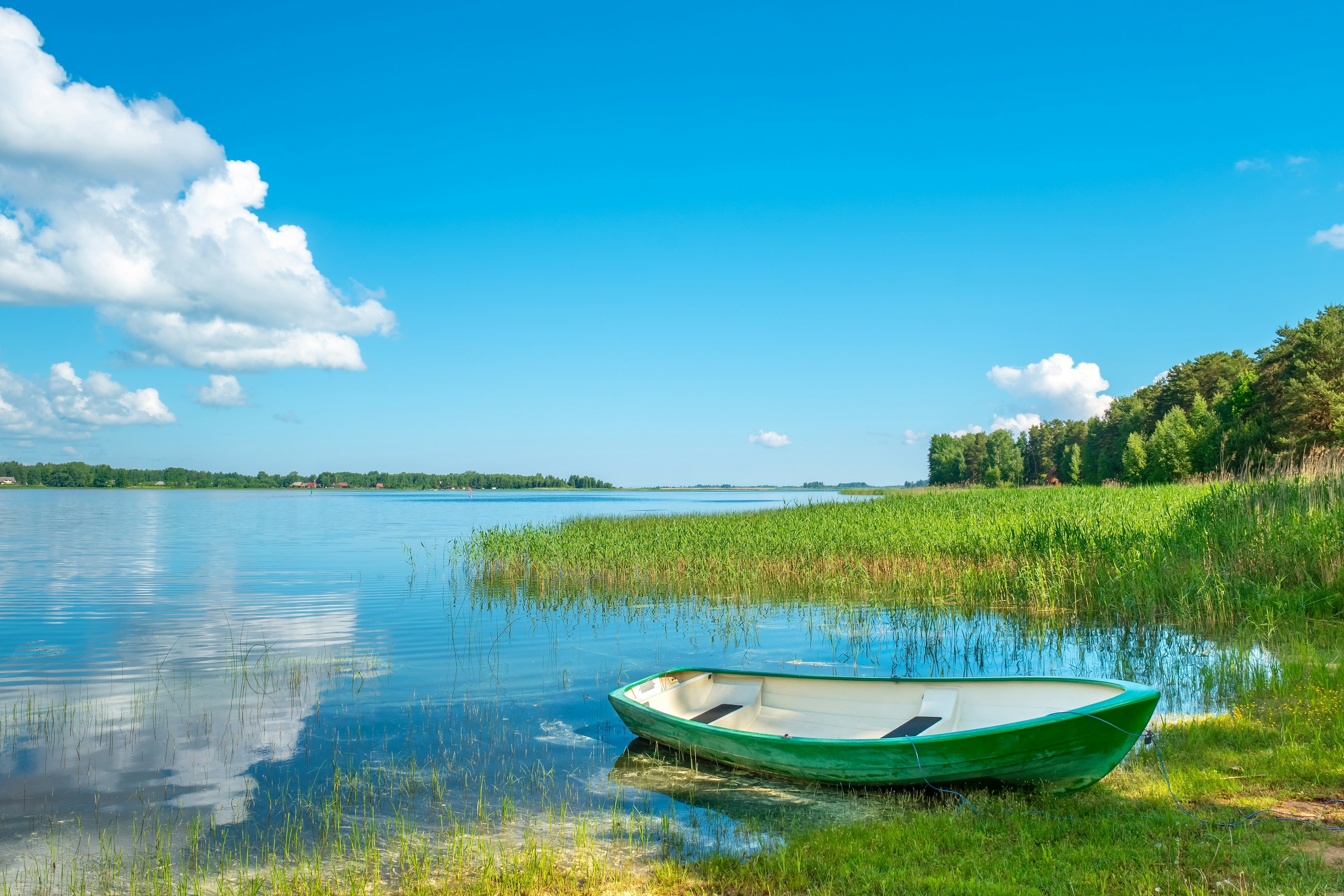 A small green rowing boat moored at the edge of a vast lake on a sunny day