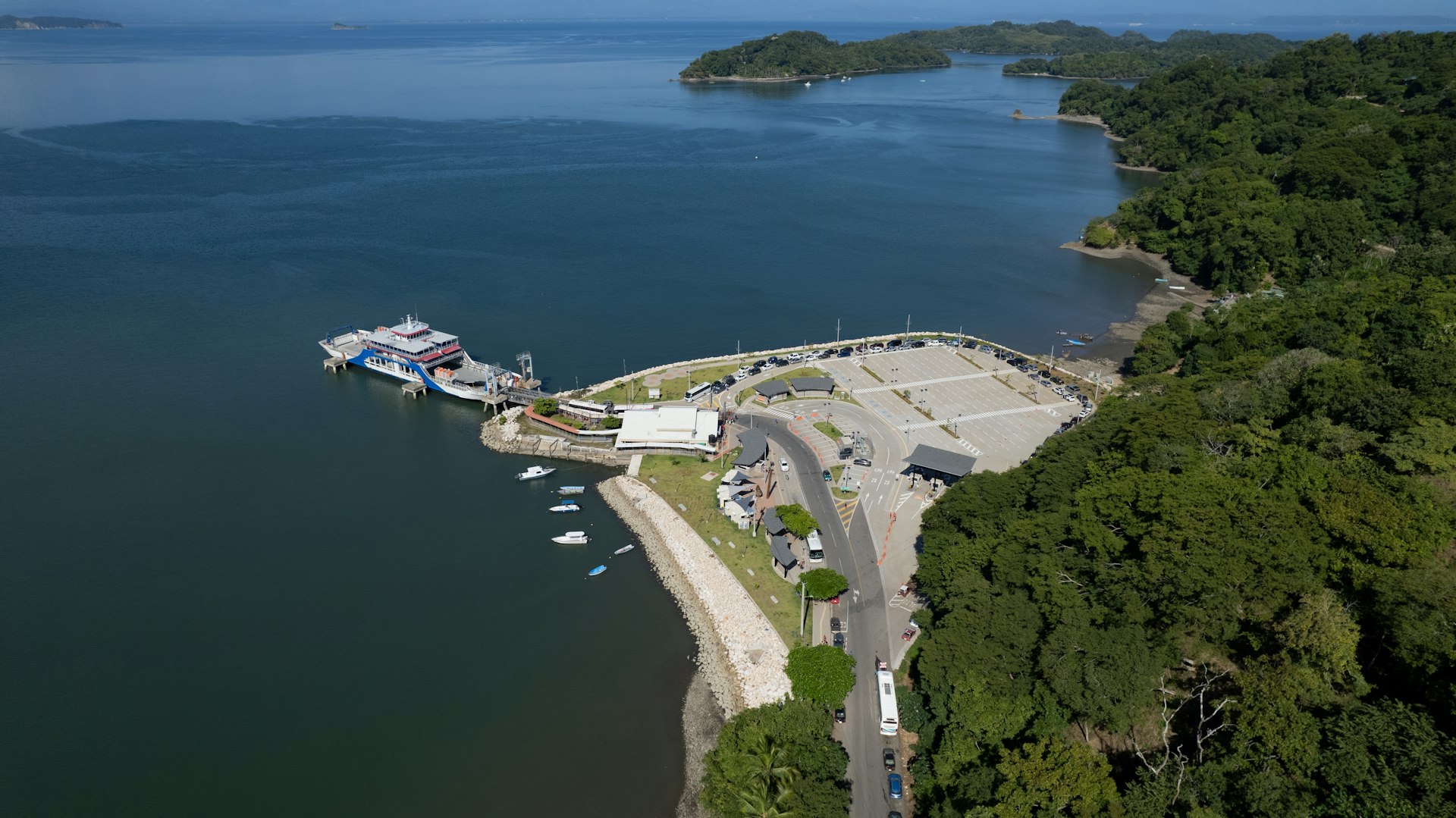 An aerial view of a ferry docked at Paquera. The water is calm and the shore is heavily forested