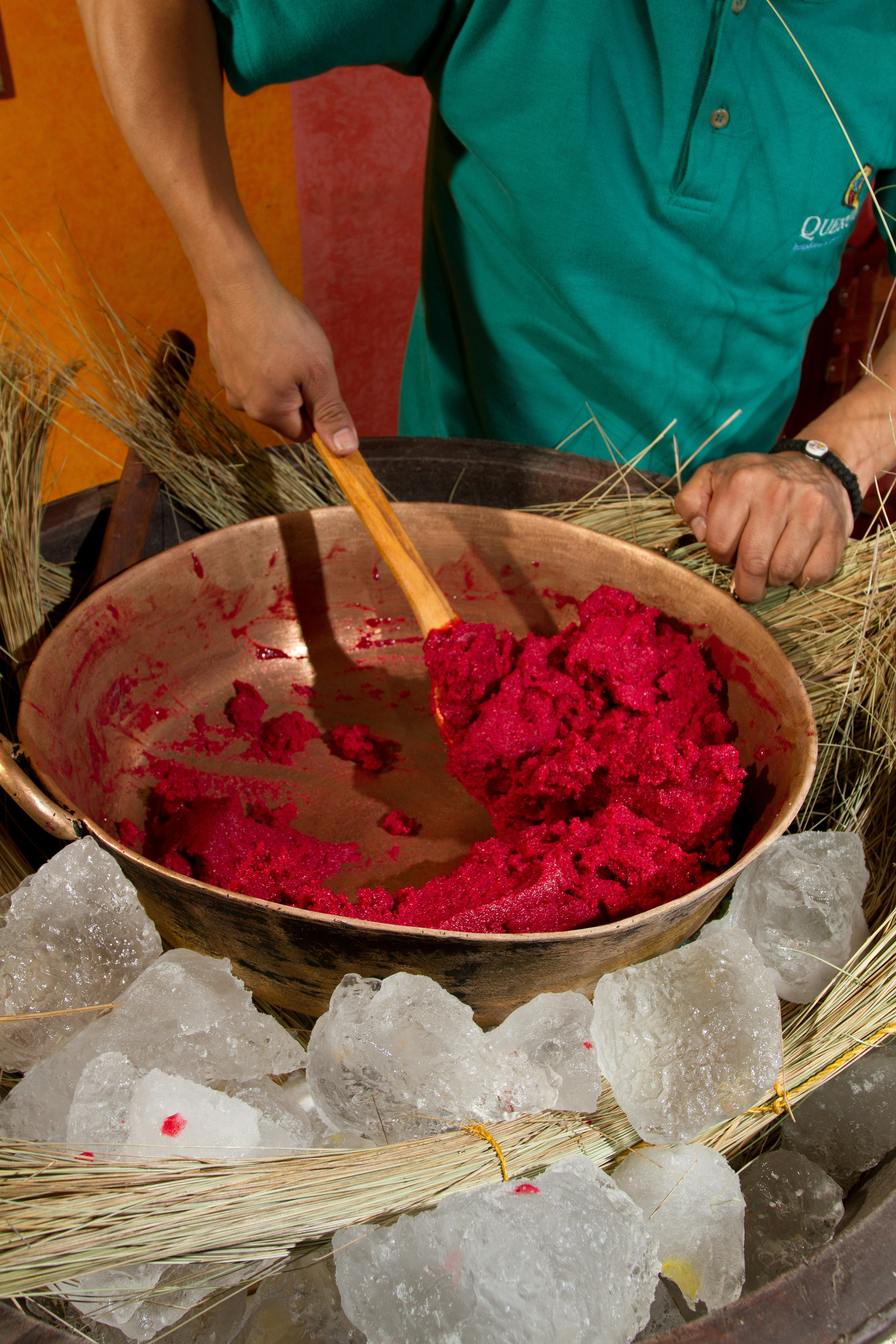 A person stirs dark pink ice cream in a bronze pot over ice in Ecuador