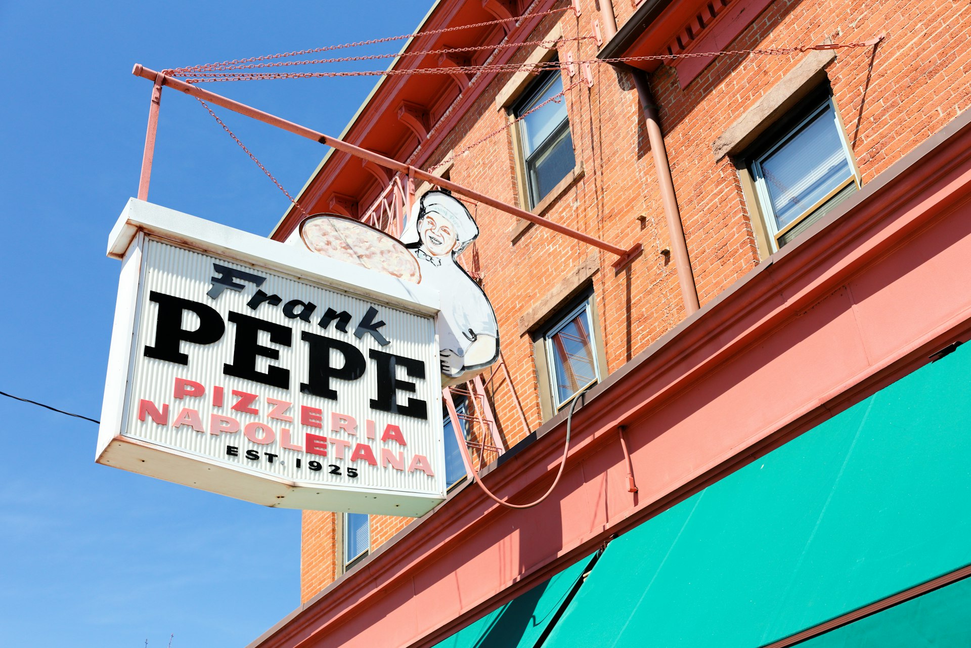 The exterior of a pizza restaurant  with a sign showing a chef that says "Frank Pepe pizza Neapolitano est 1925"