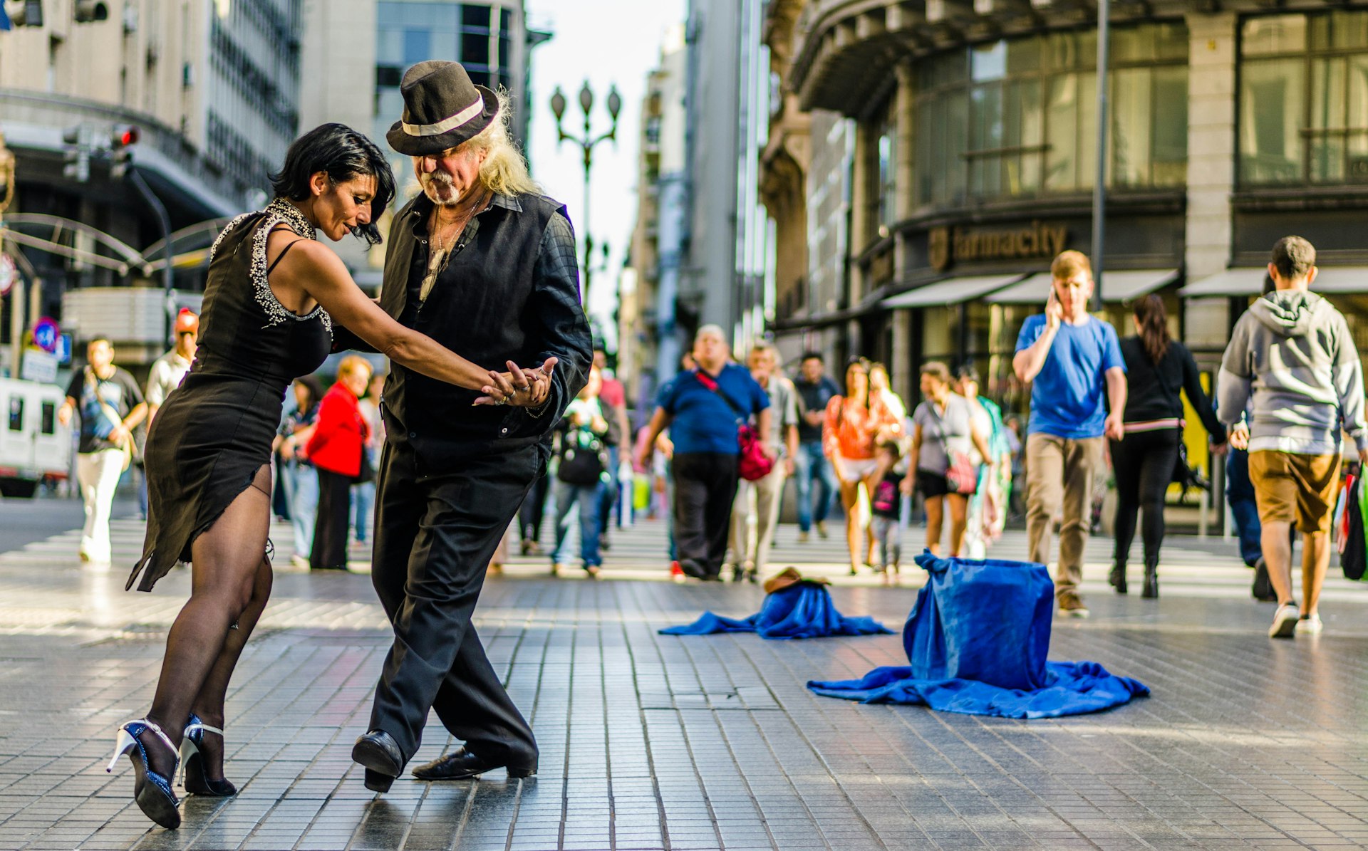 A couple dressed all in black dance a tango together in the street with some people looking on