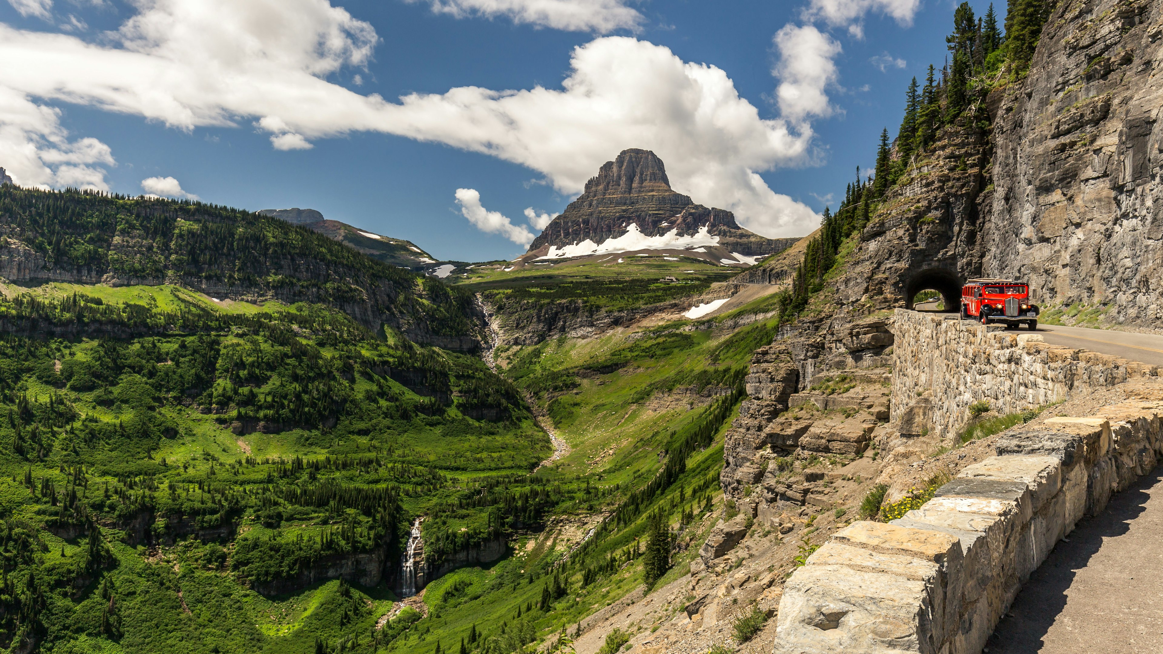 Vintage red car on a mountainous road in the Glacier National Park, with green-covered mountains in the background