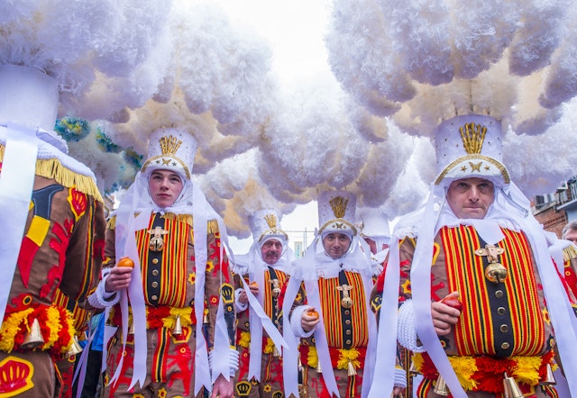 People in elaborate costumes that cover their bodies and heads stand in a smoky environment as part of a carnival parade