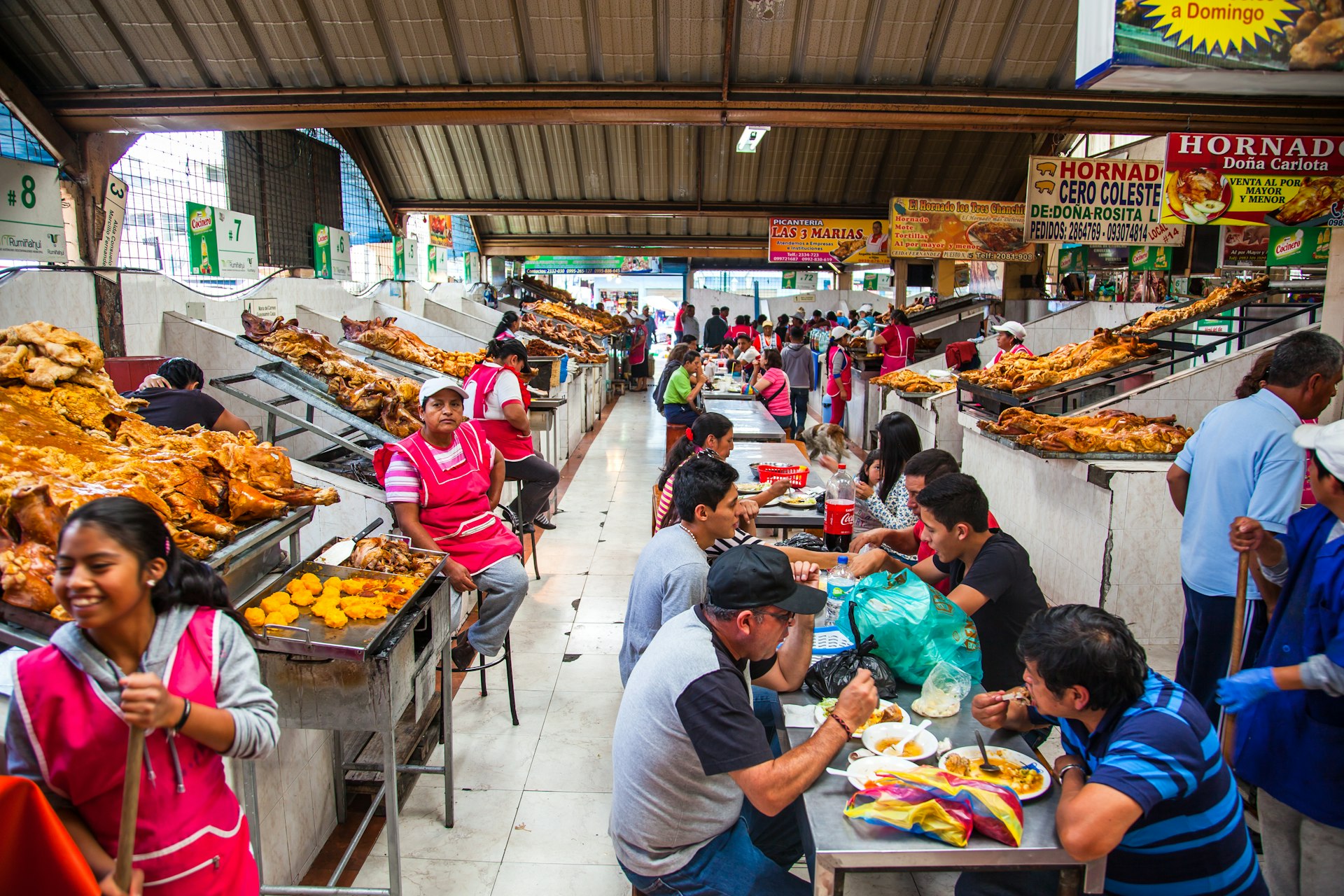 People eat pork dishes at long tables in a local market in Ecuador