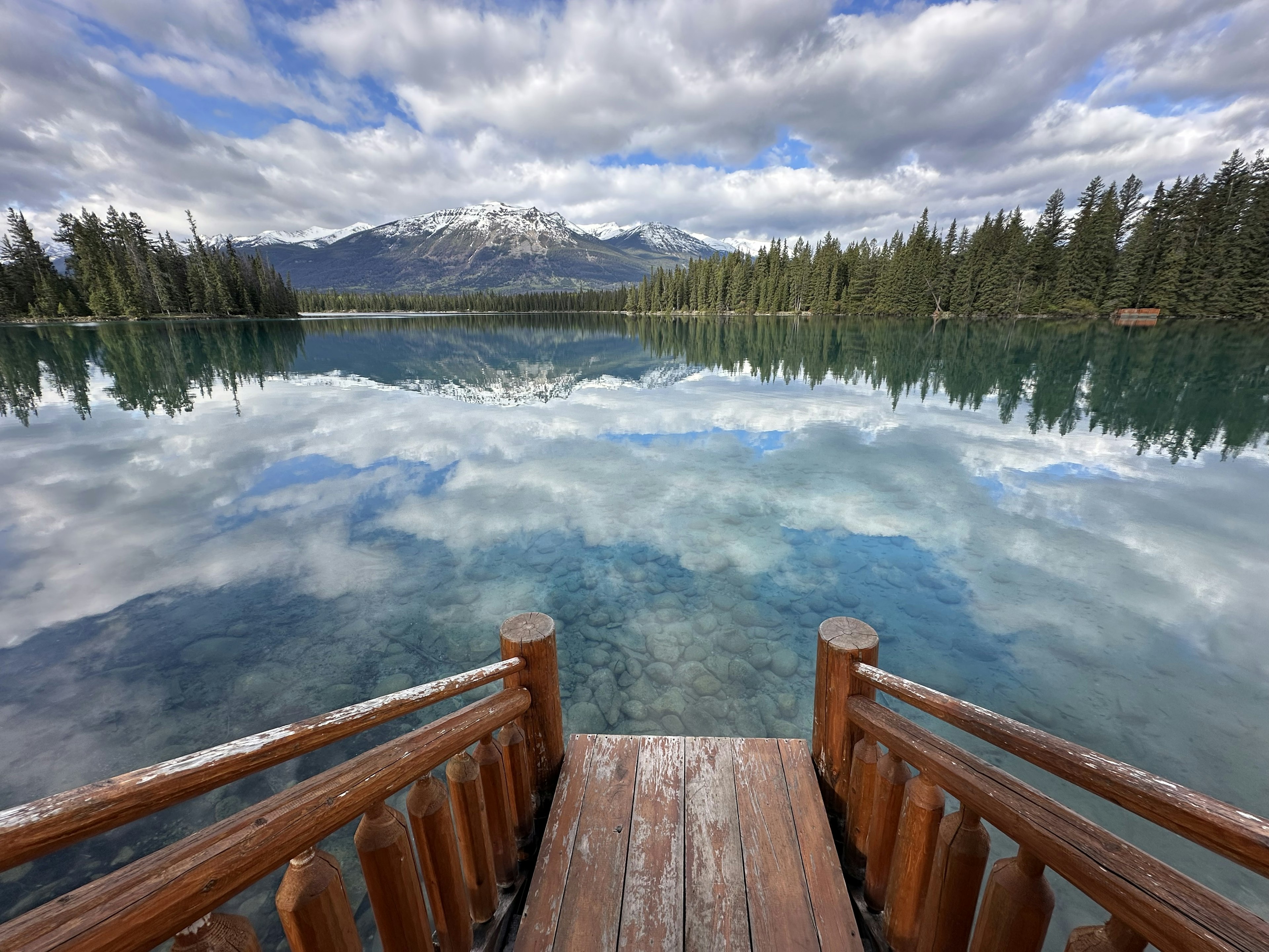 An alpine lake surrounded by trees giving an almost perfect reflection of a distant mountain