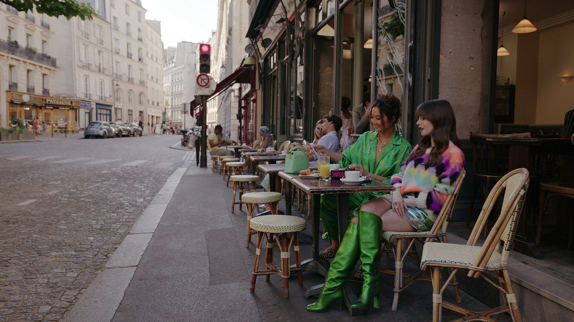 Two women sit at pavement tables outside a cafe 