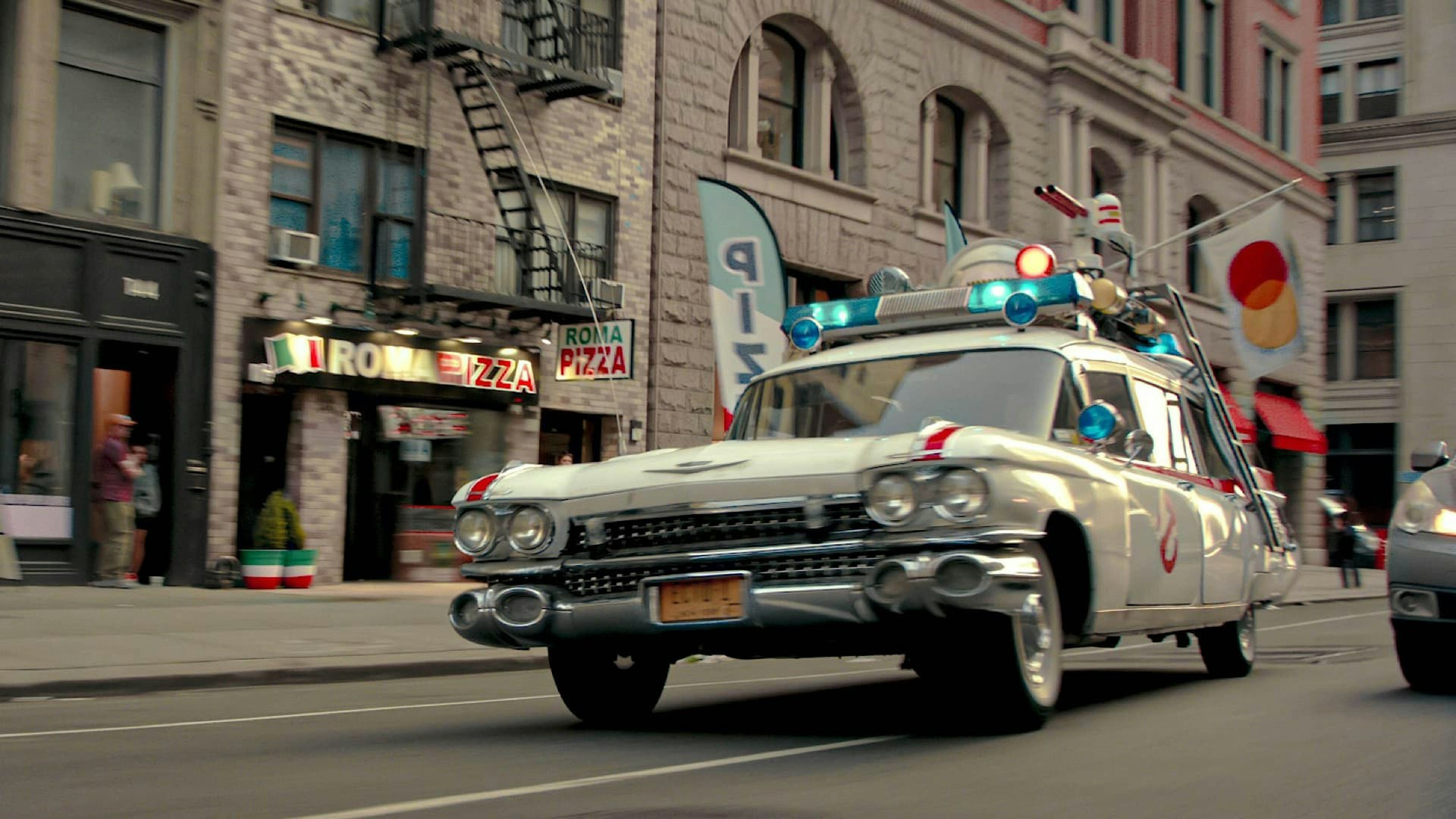 A vehicle resembling a police car but with extra lights and guns mounted on the roof speeds through a city street