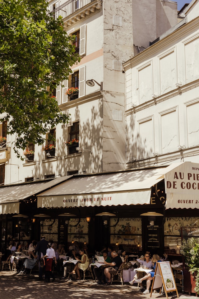 People sit at a pavement cafe under an awning at iconic Paris restaurant Au Pied de Cochon