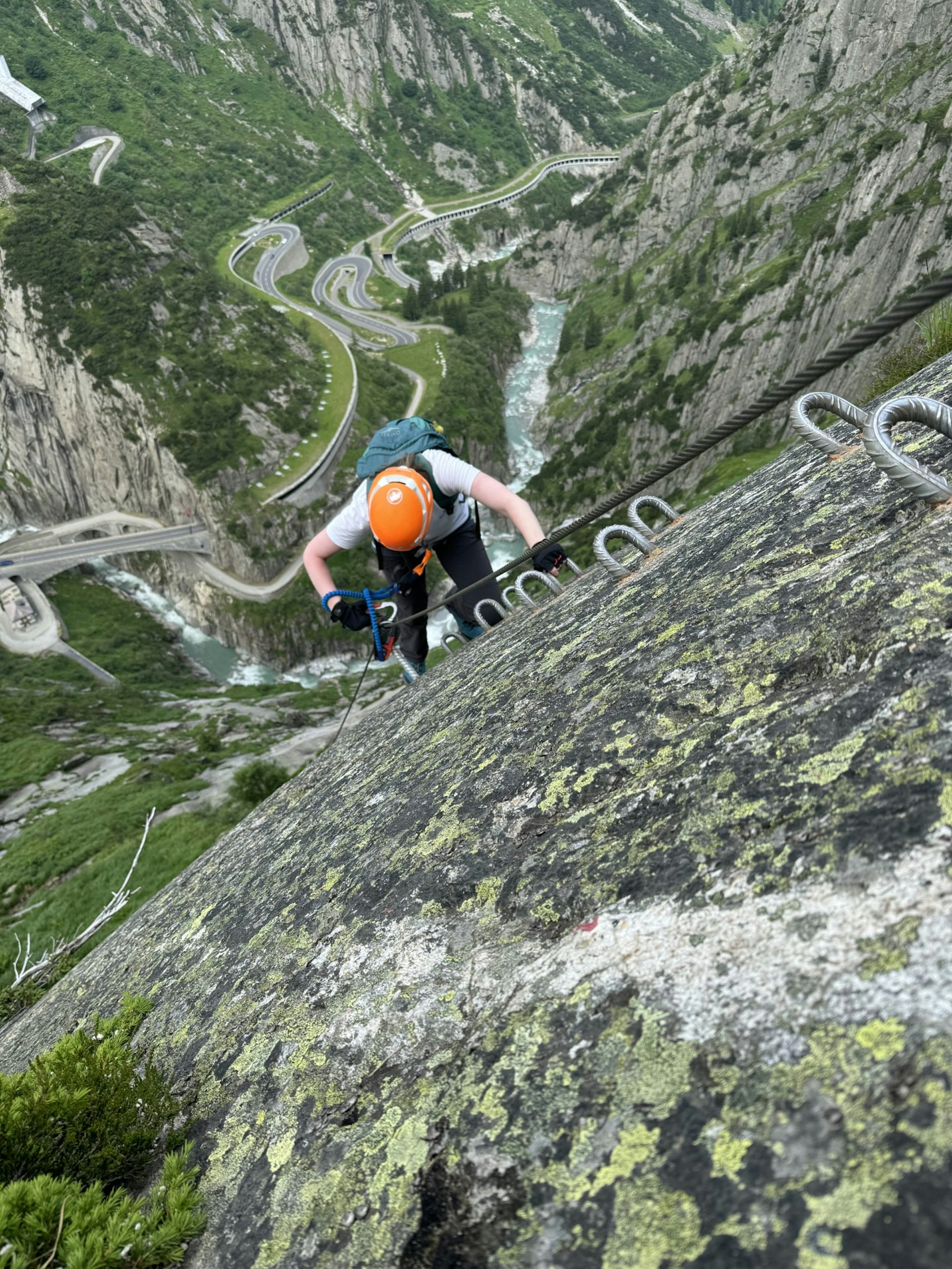 A climber clambers up a sheer cliff using cables and rungs that are anchored into the rock face