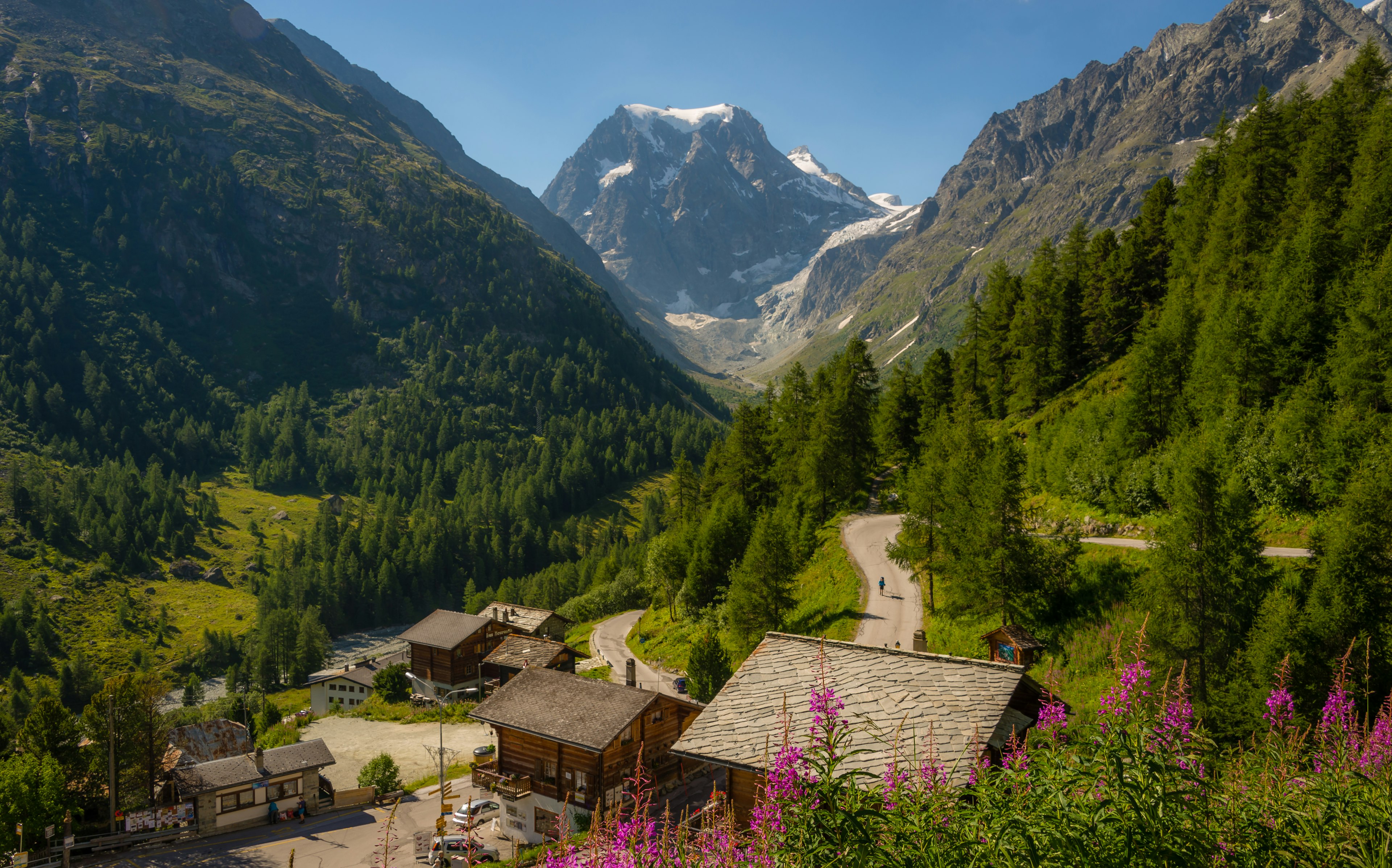 A trekker walks along a wooden-chalets-lined road that leads into the mountains