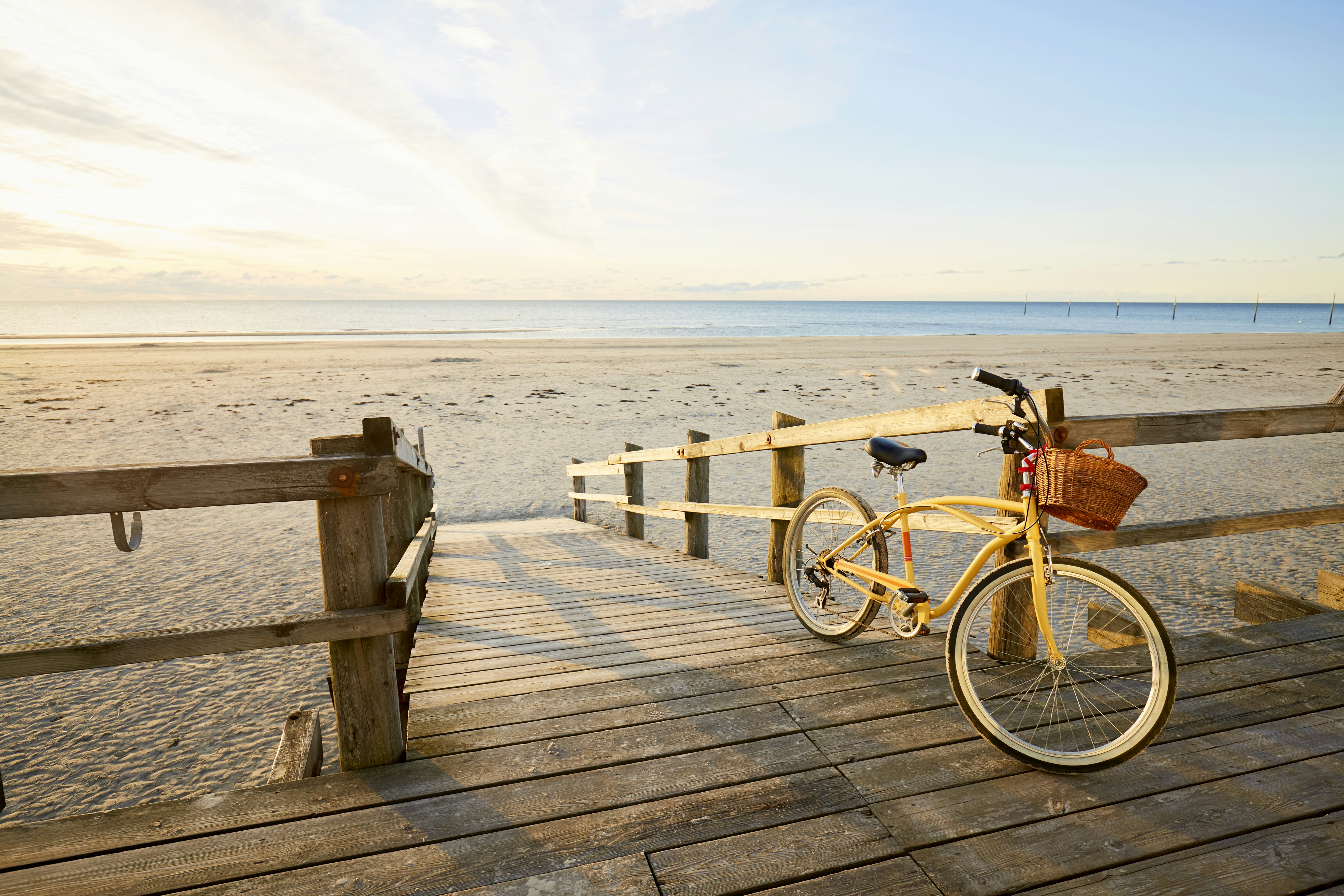 A yellow bicycle leans against wooden railings at the top of a sandy beach as the sun rises