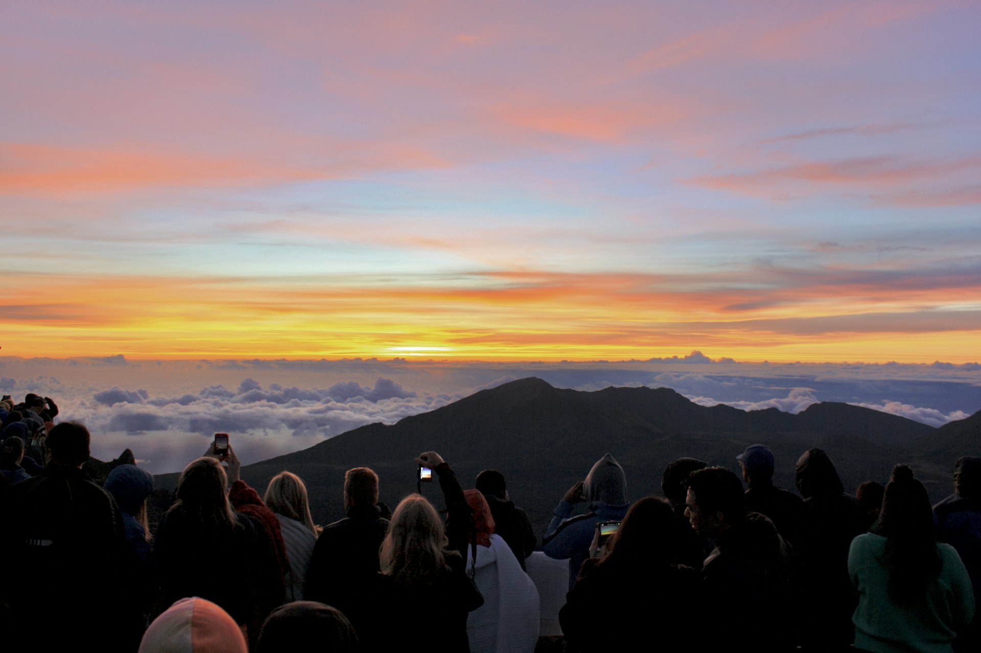 A crowd of people standing on the Haleakalā summit at dawn, silhouetted against the sunrise