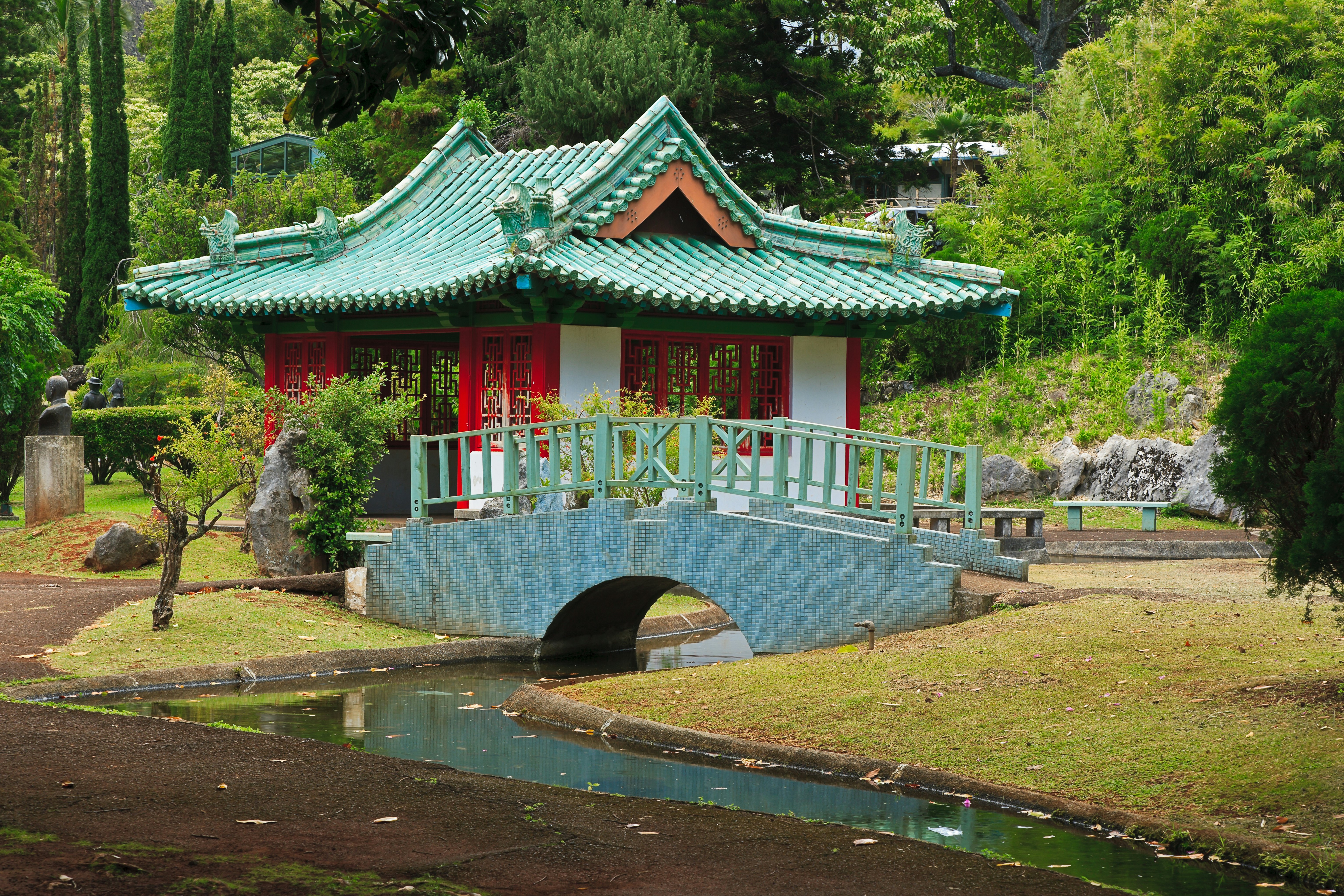 A red and teal temple and bridge sit in the greenery of Kepaniwai Park in Maui