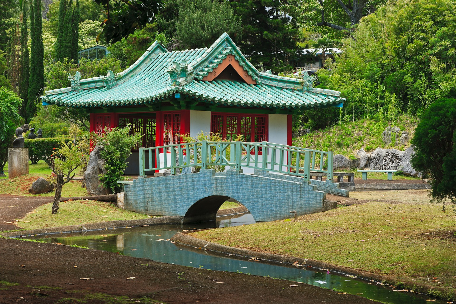 A red and teal temple and bridge sit in the greenery of Kepaniwai Park in Maui