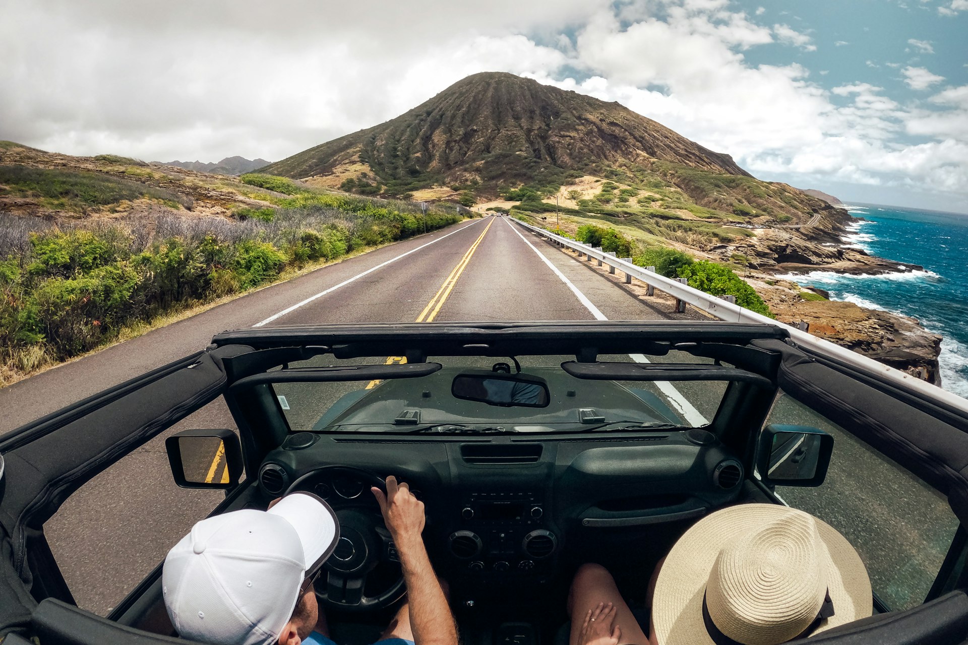 Two people driving a convertible car along a coastal road on Maui