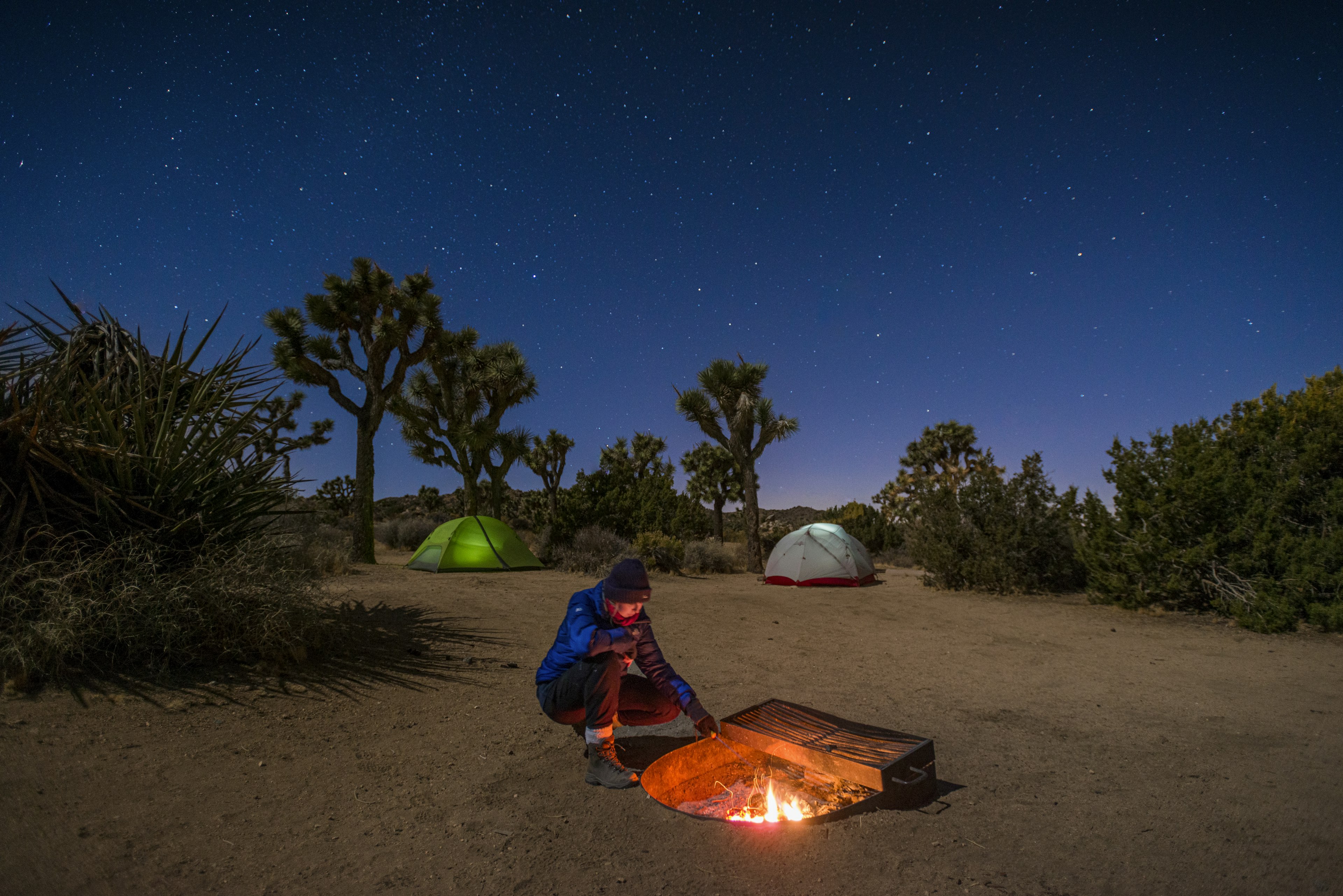 A woman stokes a camp fire near her tent at night in Joshua Tree National Park, California, USA