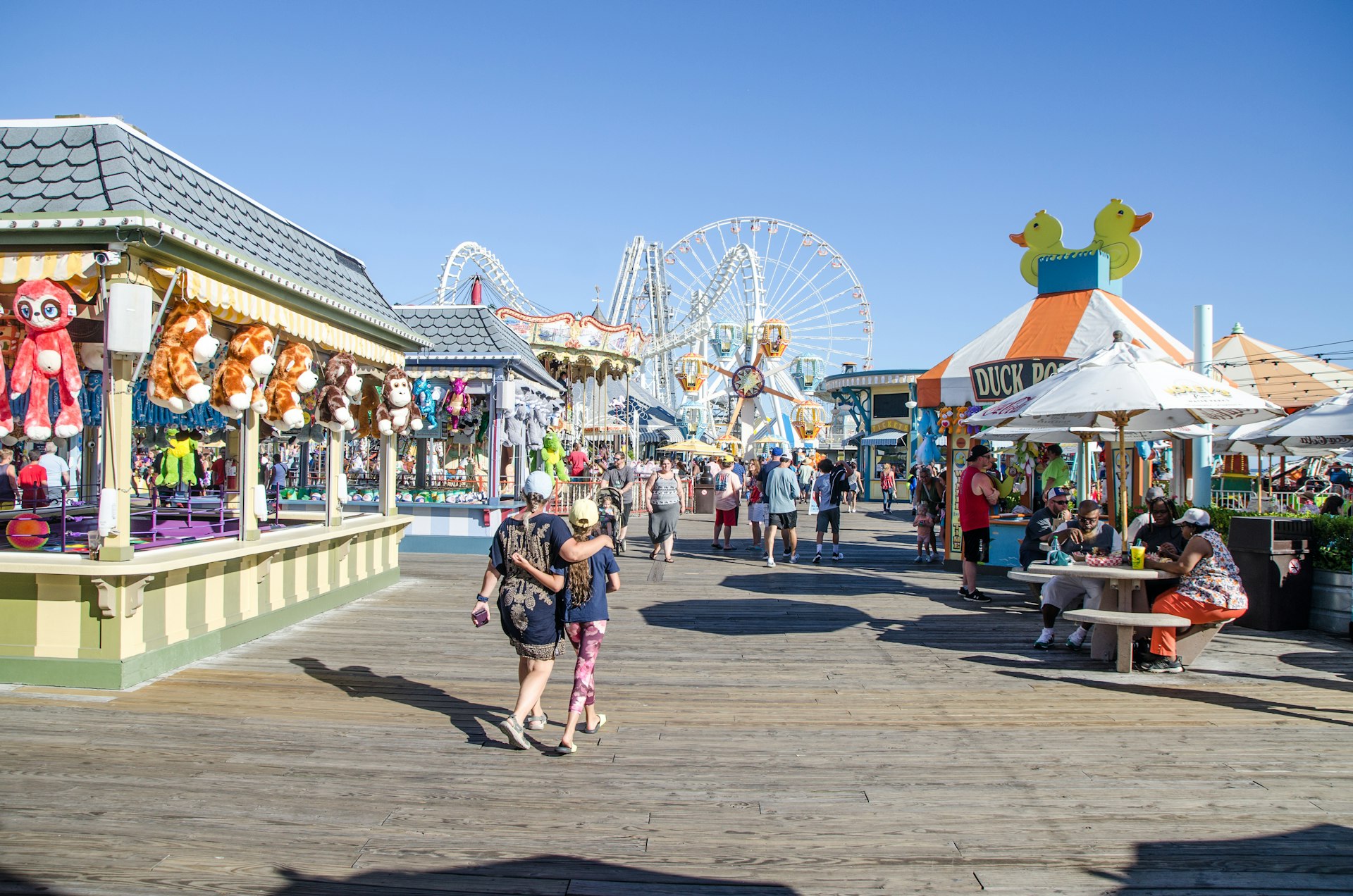 Two vacationers are walking through an amusement park with fairground games and rides in Wildwood, New Jersey