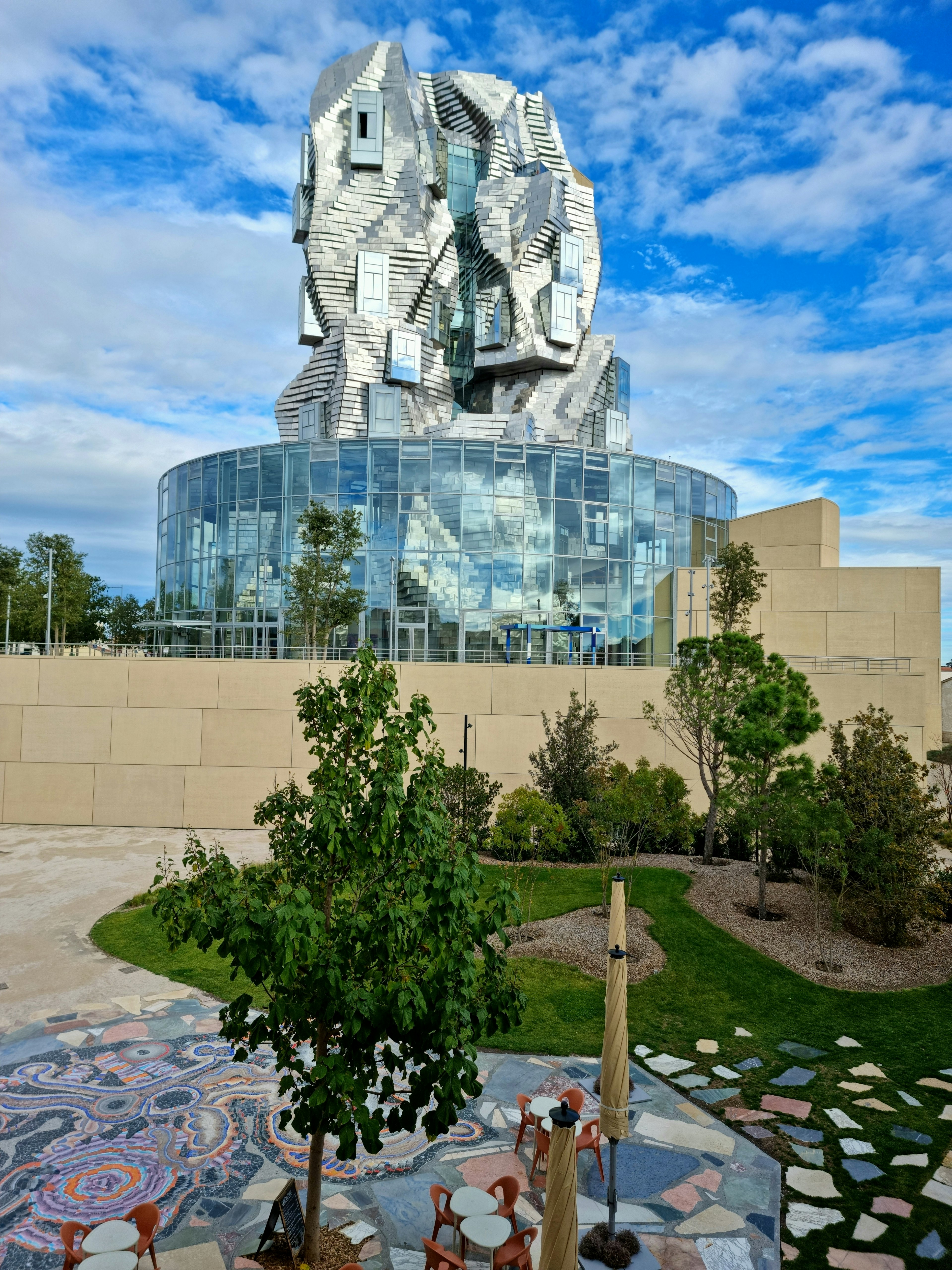 A tall modern building that has a circular base made from glass with a twisting metallic tower rising from it.