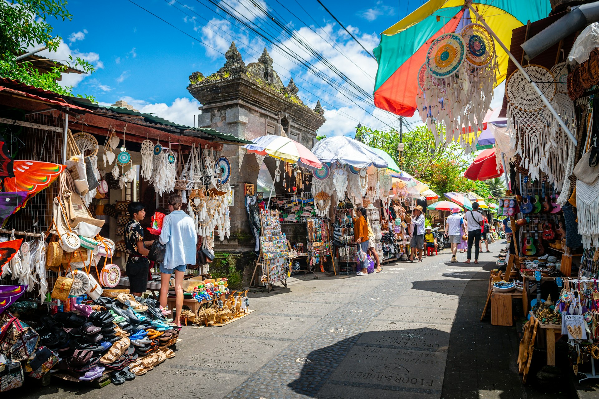 Many people peruse the souvenir items at market stalls lining a street in Ubud, Bali